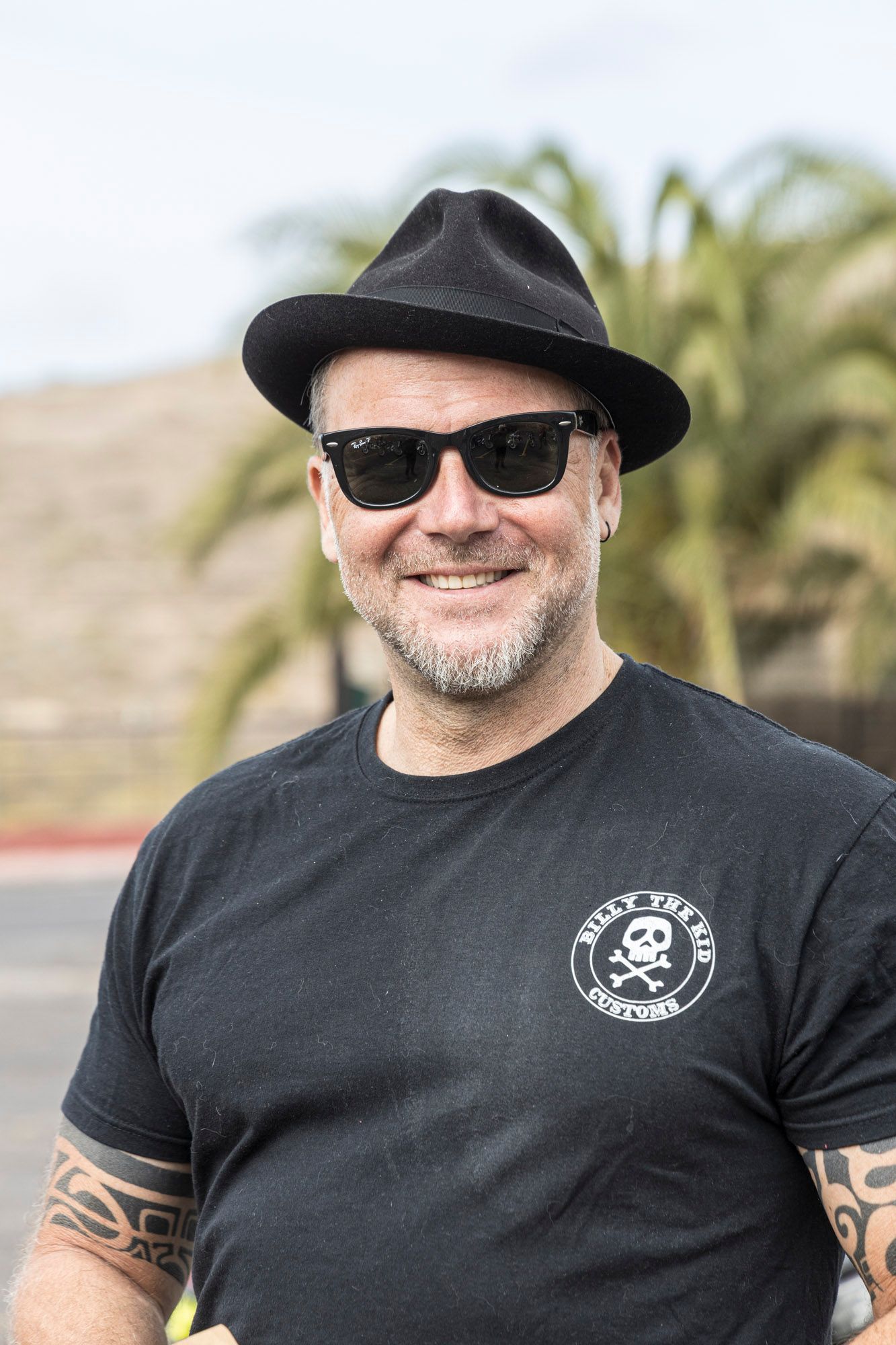 A man wearing a hat and sunglasses is smiling for the camera.