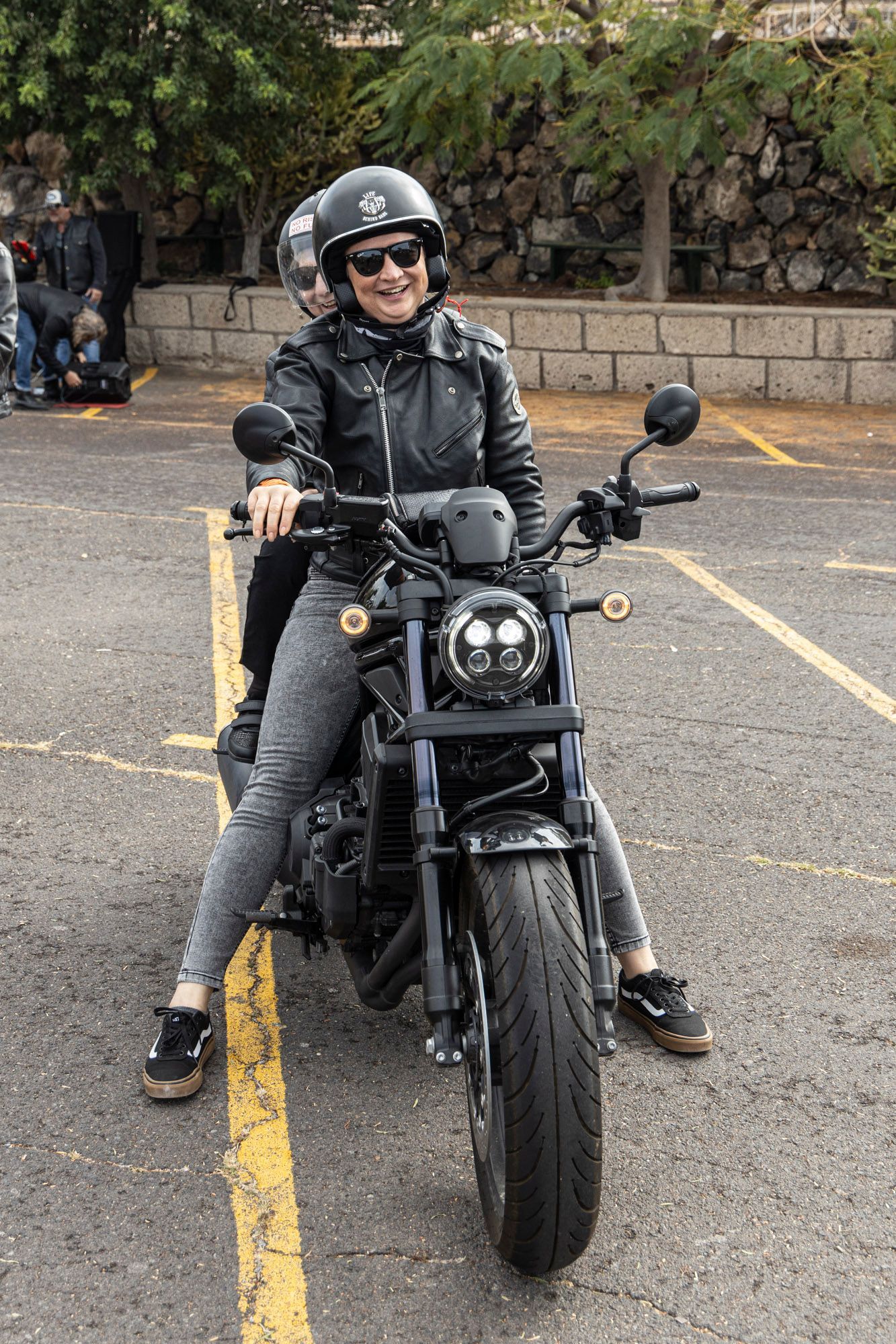 A woman is sitting on a motorcycle in a parking lot.