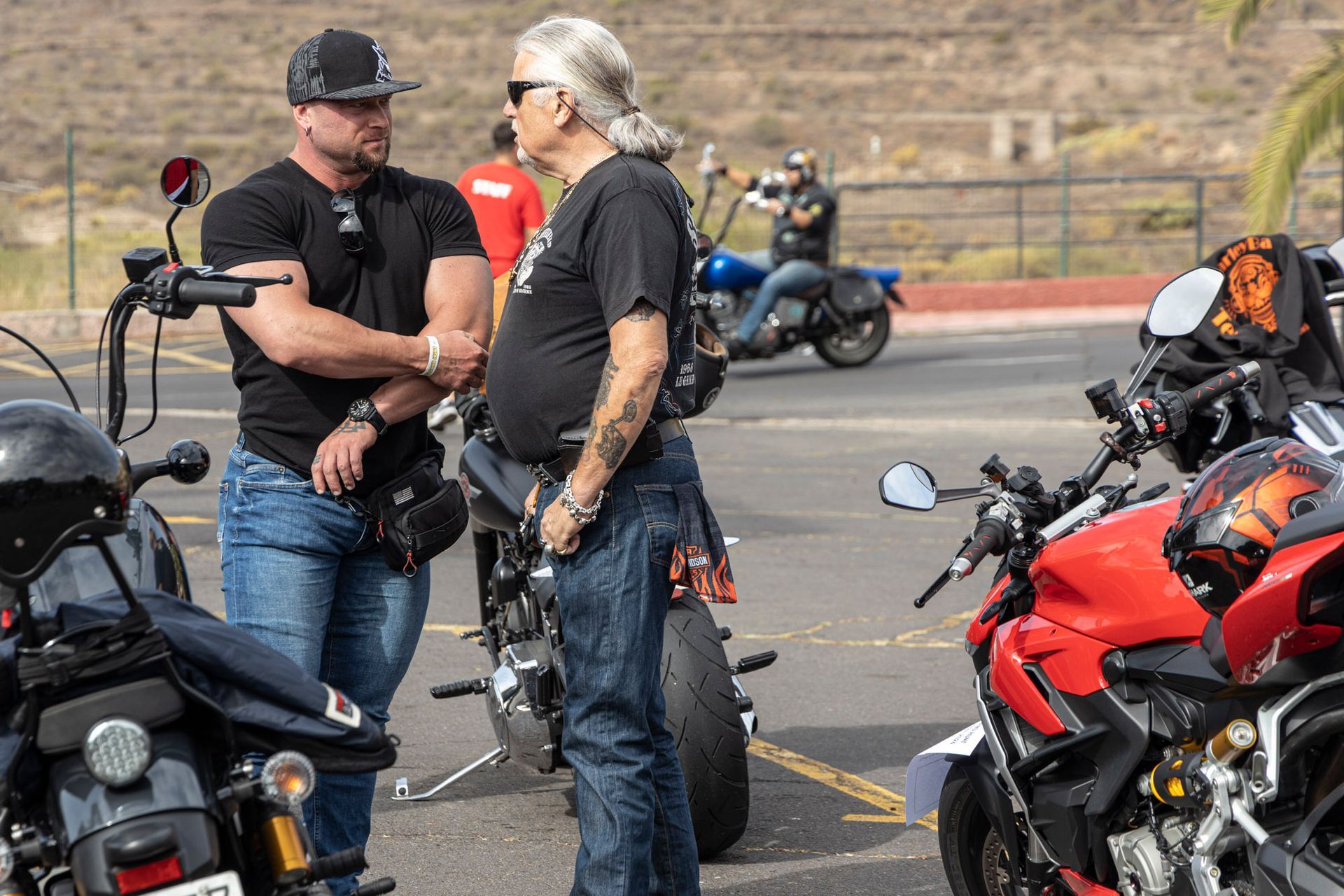 Two men are standing next to motorcycles in a parking lot.