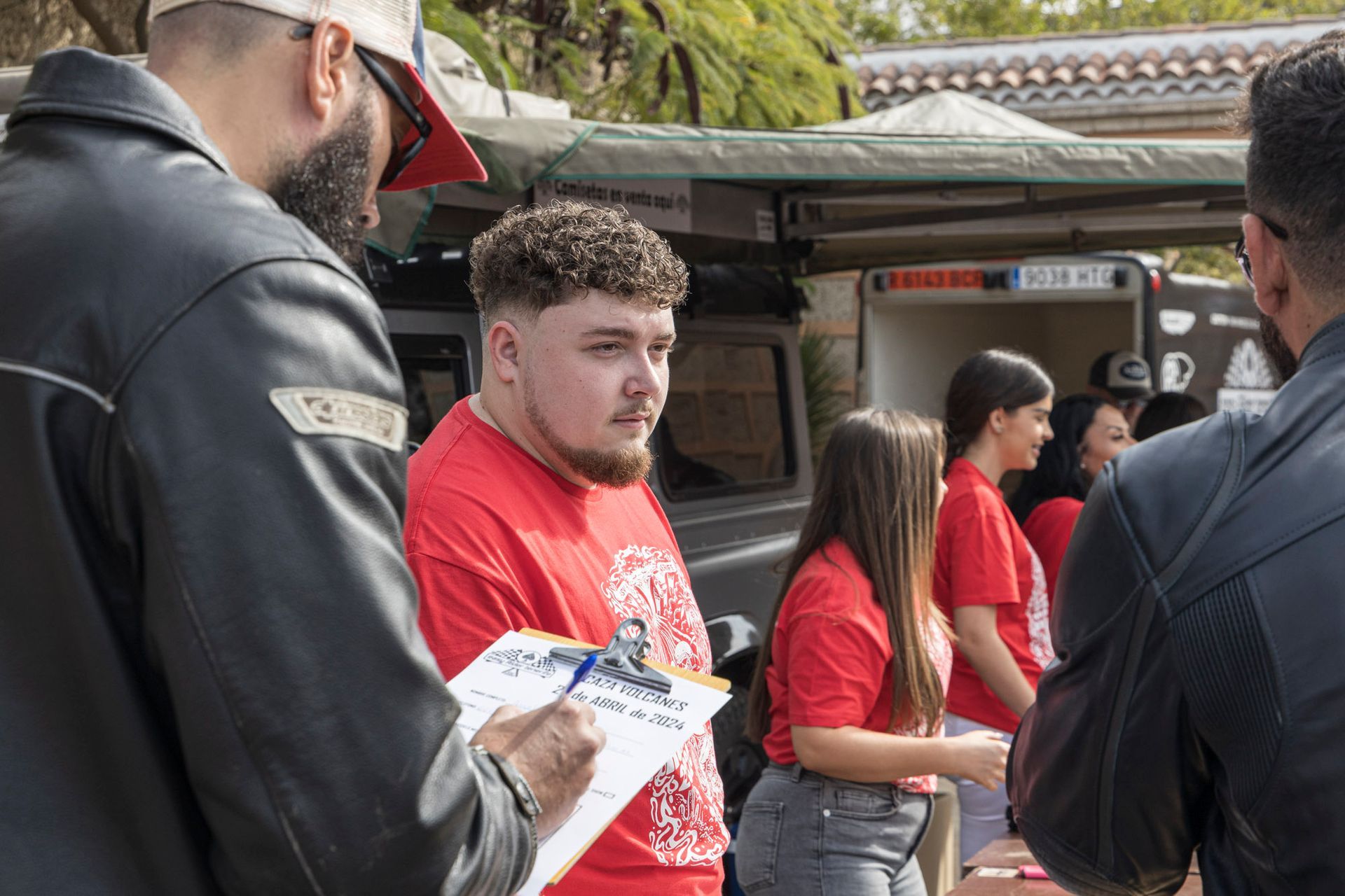 A man is writing on a clipboard while standing next to a group of people.