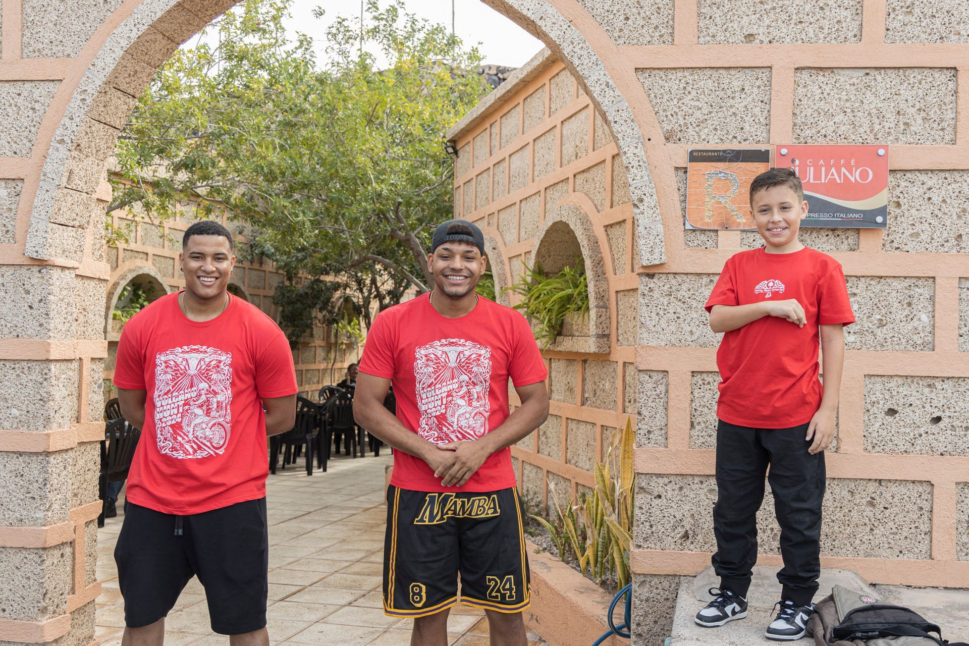 Three men in red shirts are standing next to each other in front of a stone archway.