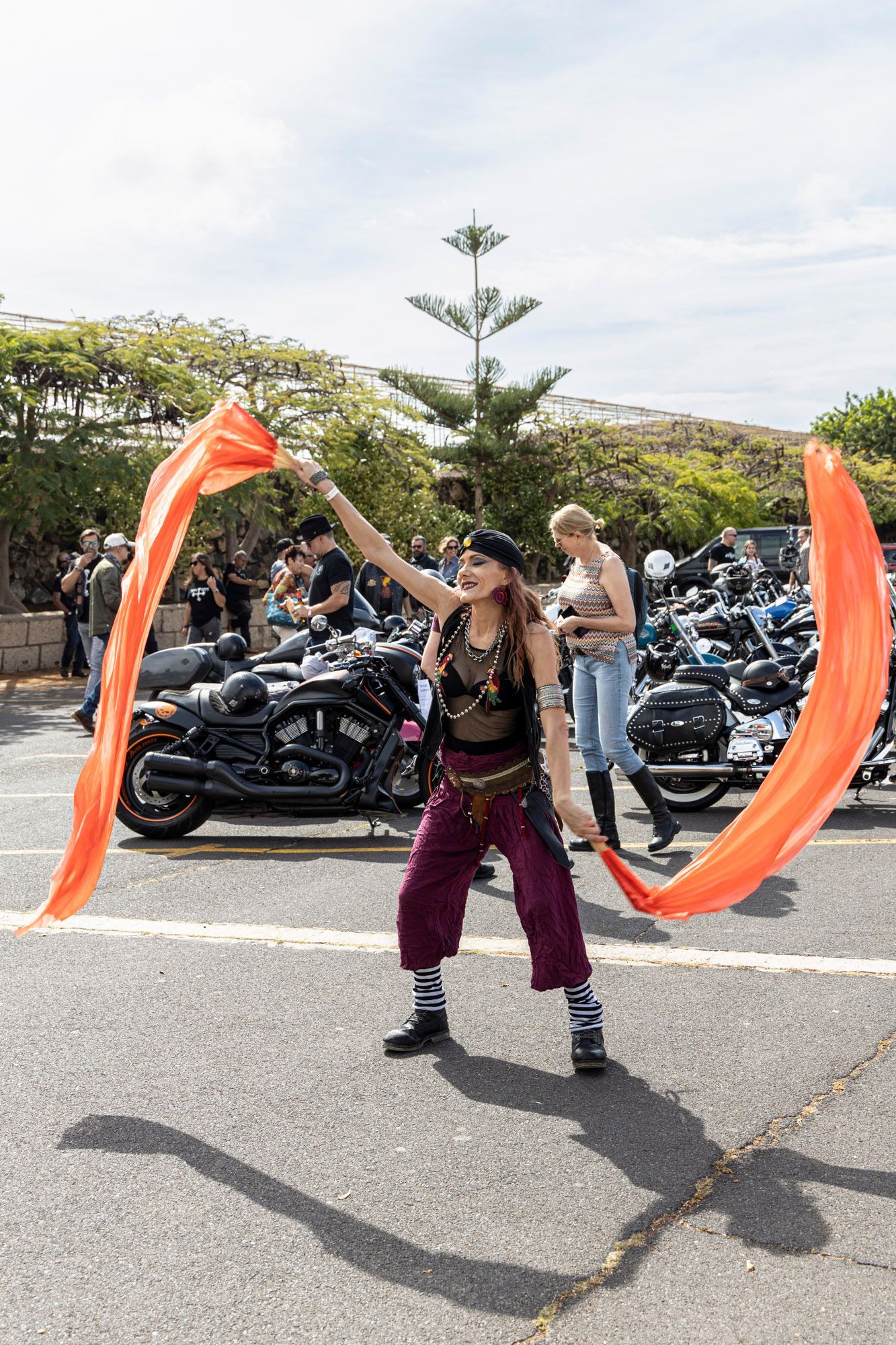 A woman in a pirate costume is holding an orange flag in front of a motorcycle parade.