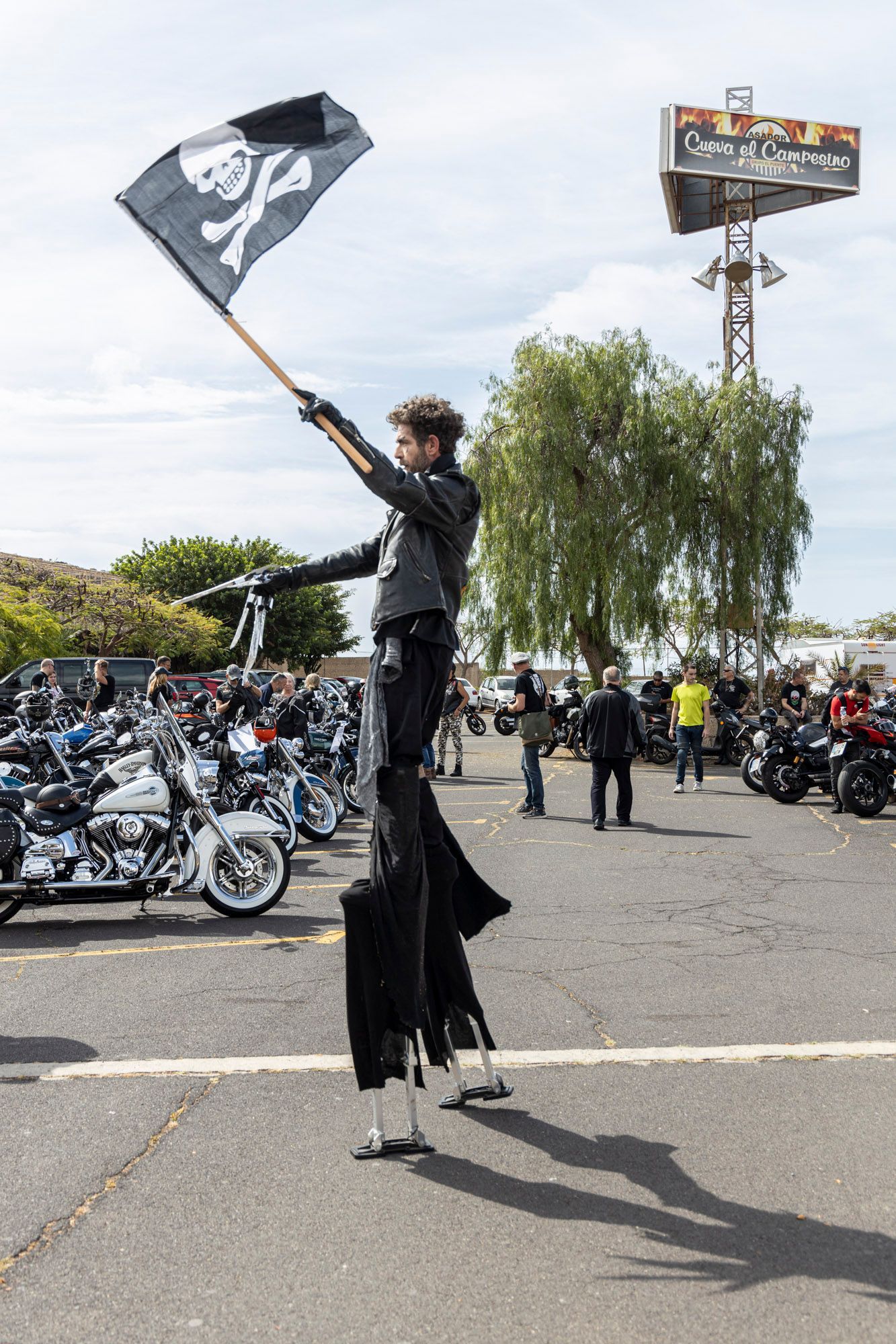 A man on stilts is holding a flag with a skull and crossbones on it.