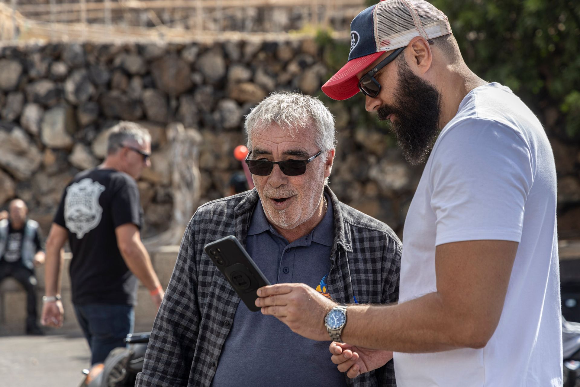 Two men are standing next to each other looking at a cell phone.