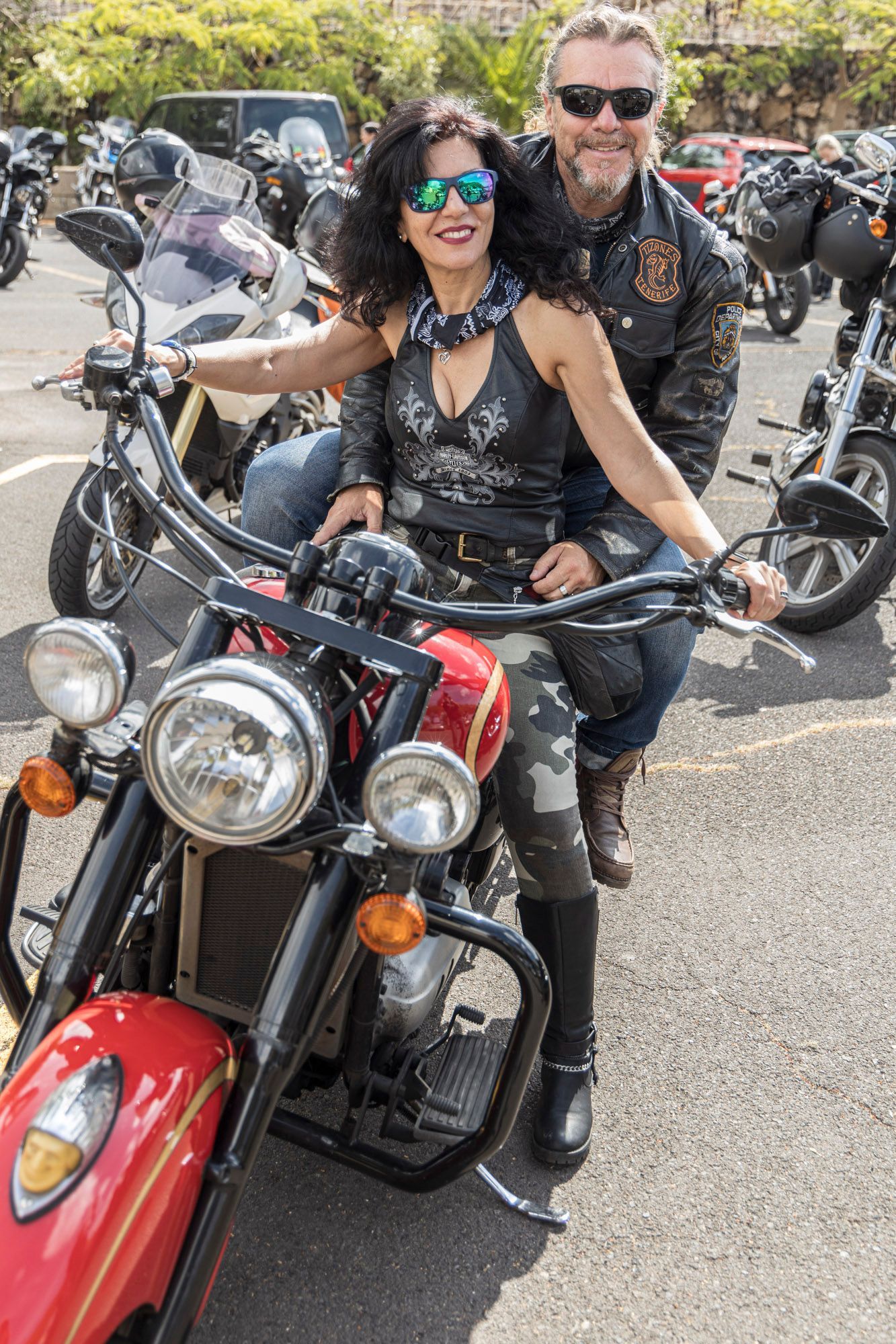 A man and a woman are sitting on a motorcycle in a parking lot.