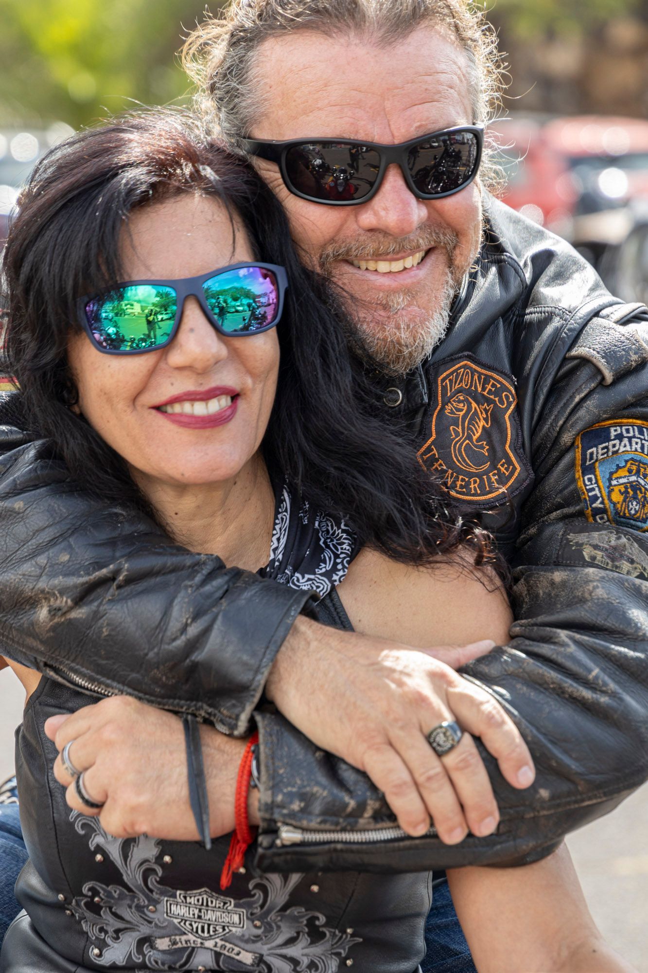 A man and a woman wearing sunglasses are hugging each other on a motorcycle.