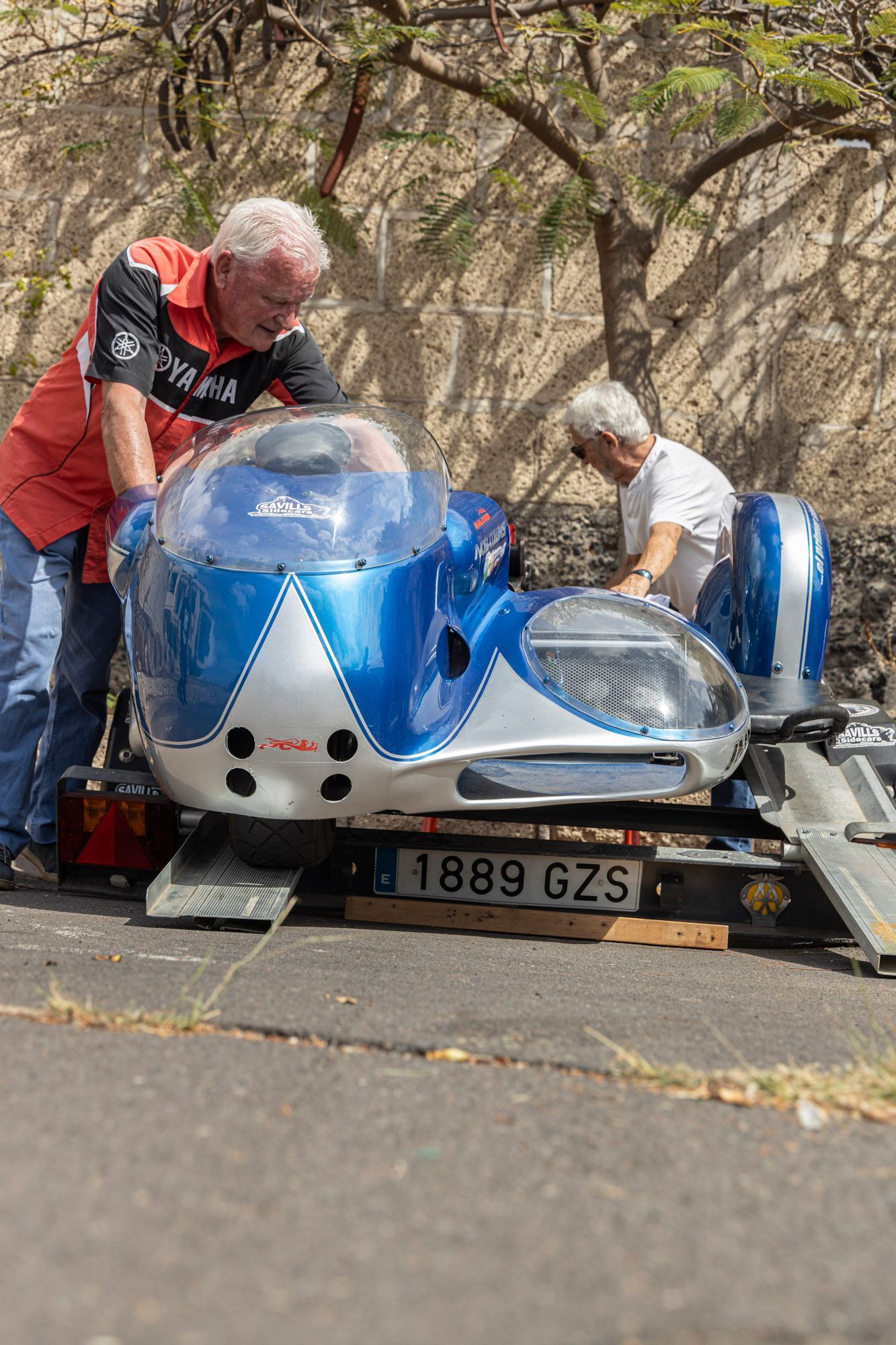 Two men are working on a blue and white sidecar motorcycle.