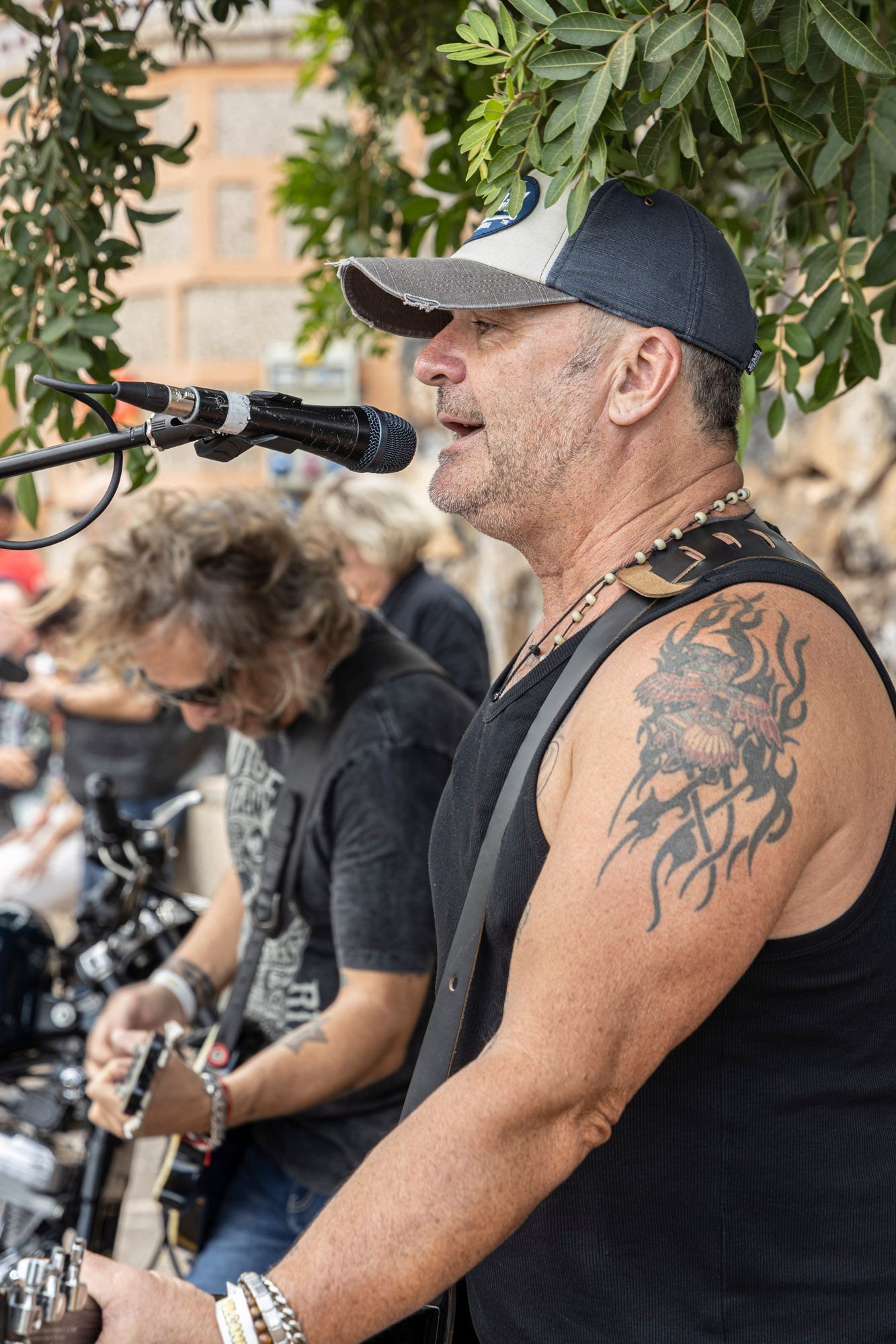 A man with a tattoo on his arm is singing into a microphone while playing a guitar.