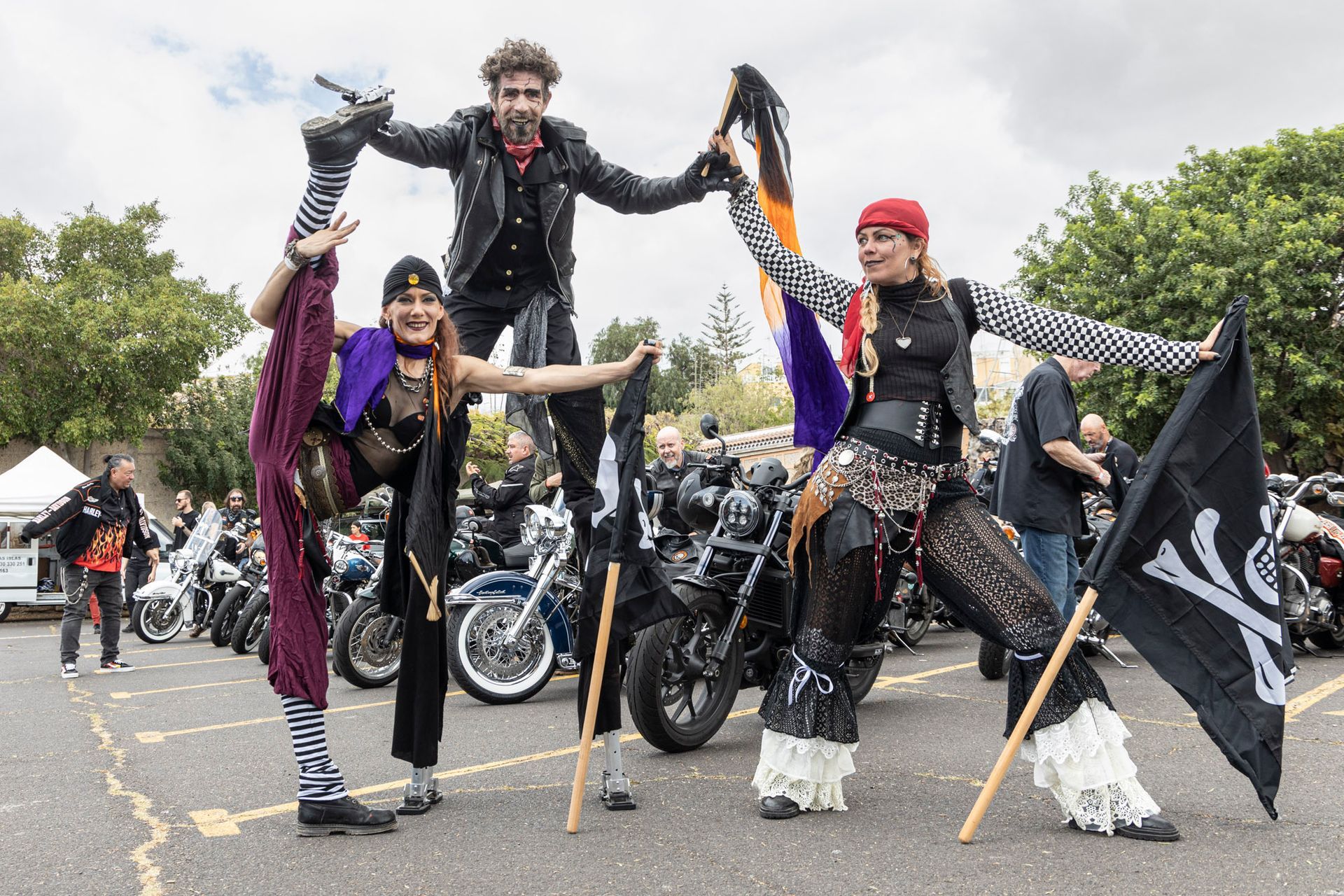 A group of people are standing on stilts in front of motorcycles.