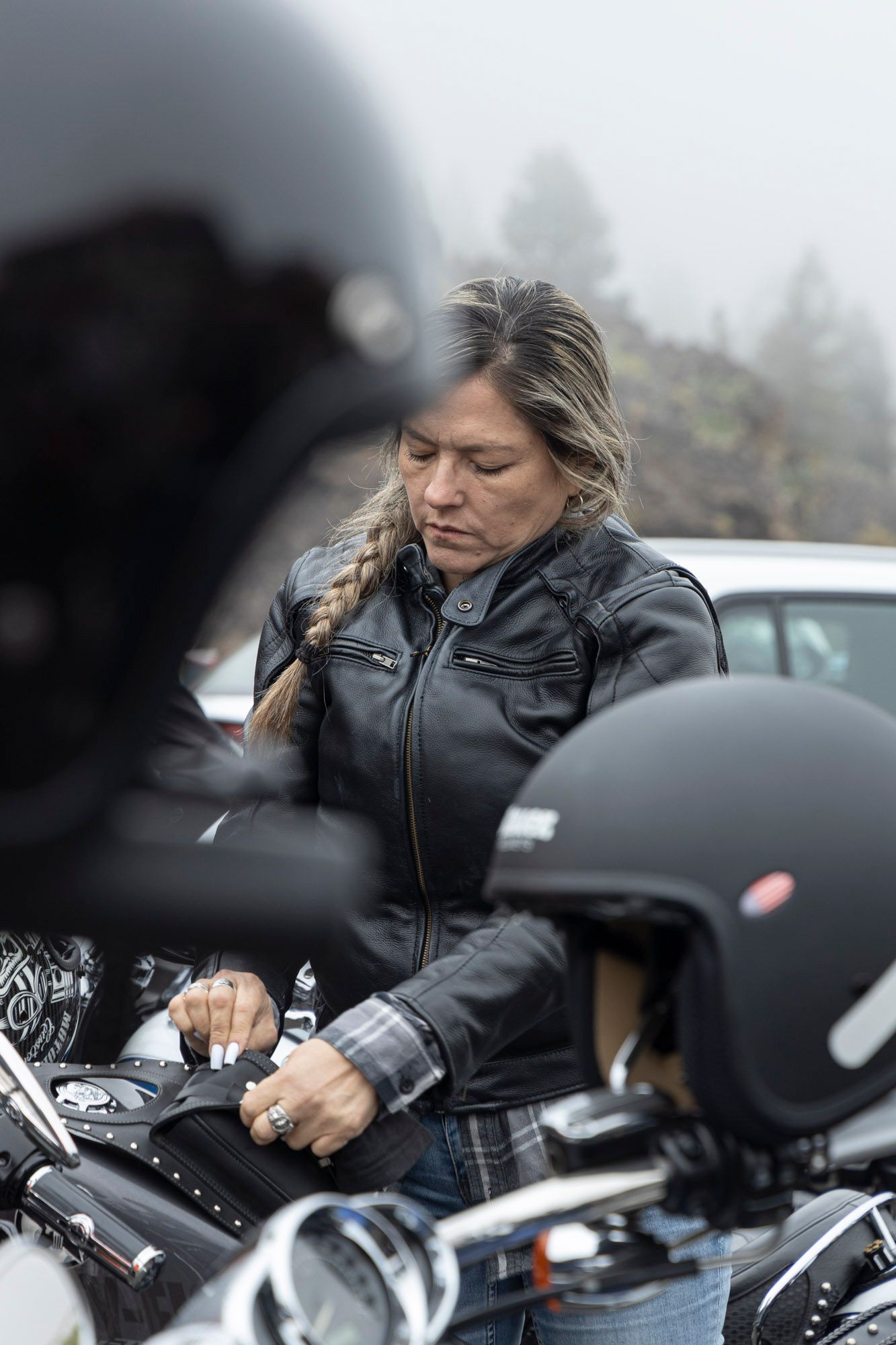 A woman is putting on a helmet on a motorcycle.