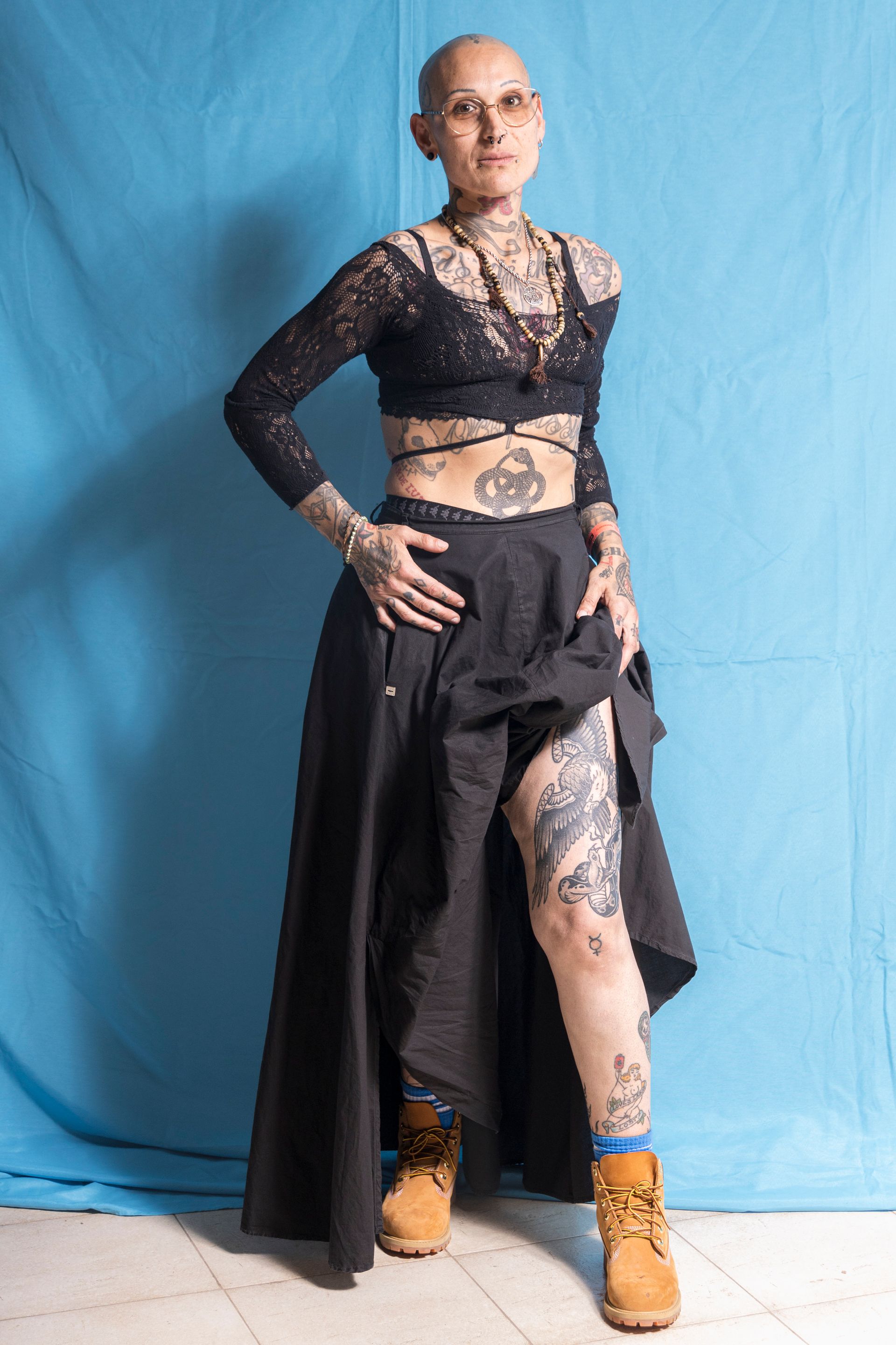 A woman with a lot of tattoos on her body is standing in front of a blue curtain.