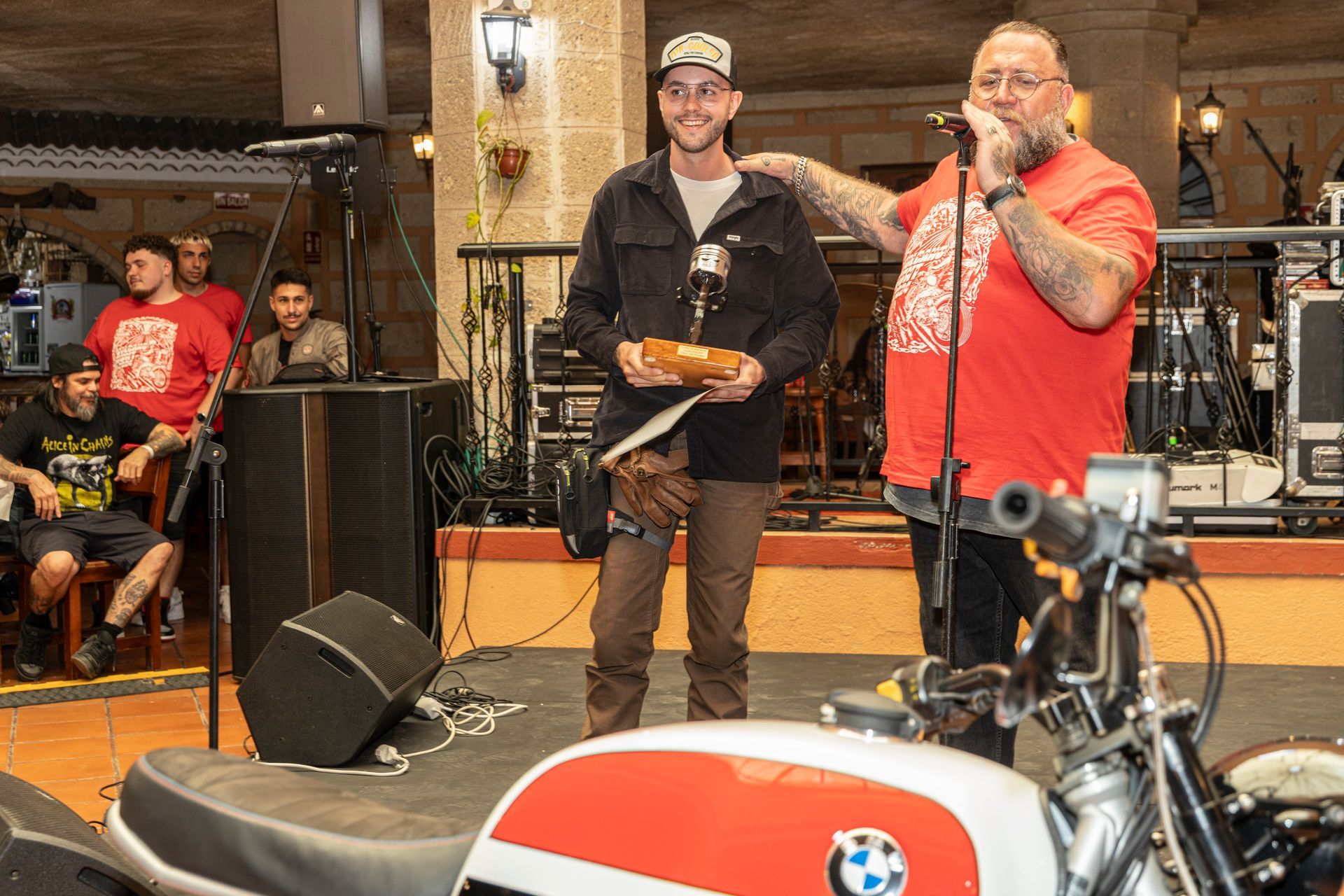 Two men are standing next to a motorcycle and one is holding a trophy.