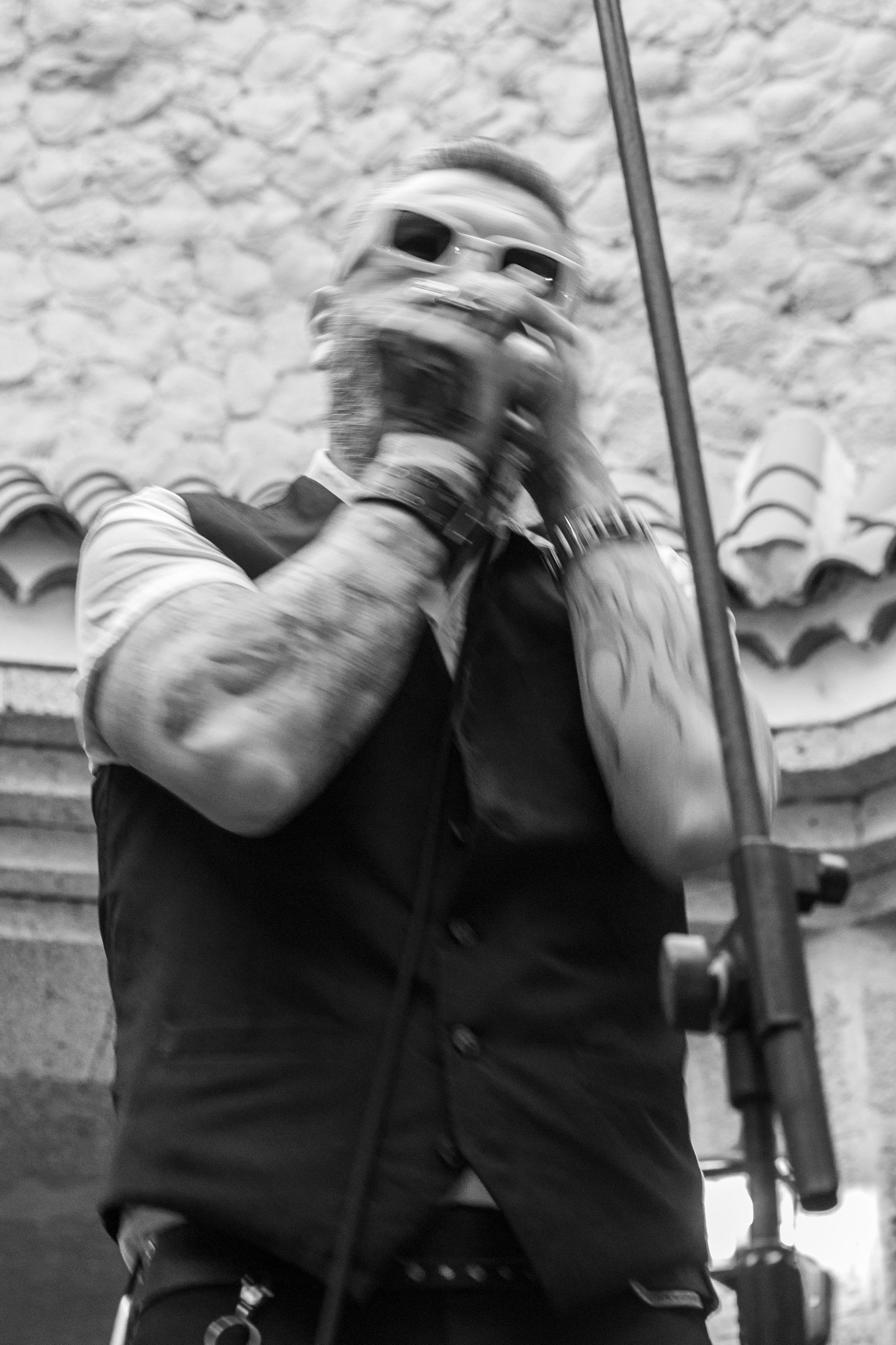 A man is singing into a microphone in front of a stone wall.