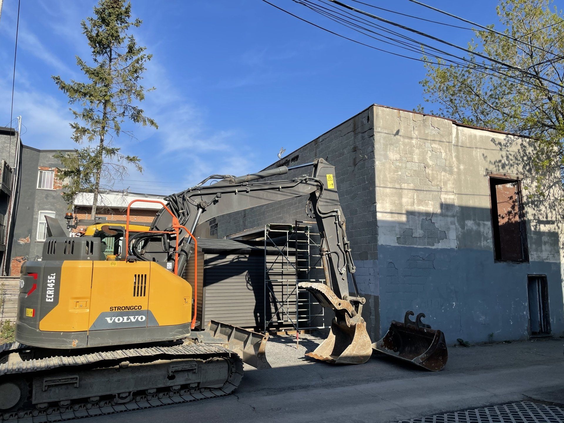 Une pelleteuse démolit un bâtiment par une journée ensoleillée. L'engin est jaune et noir.