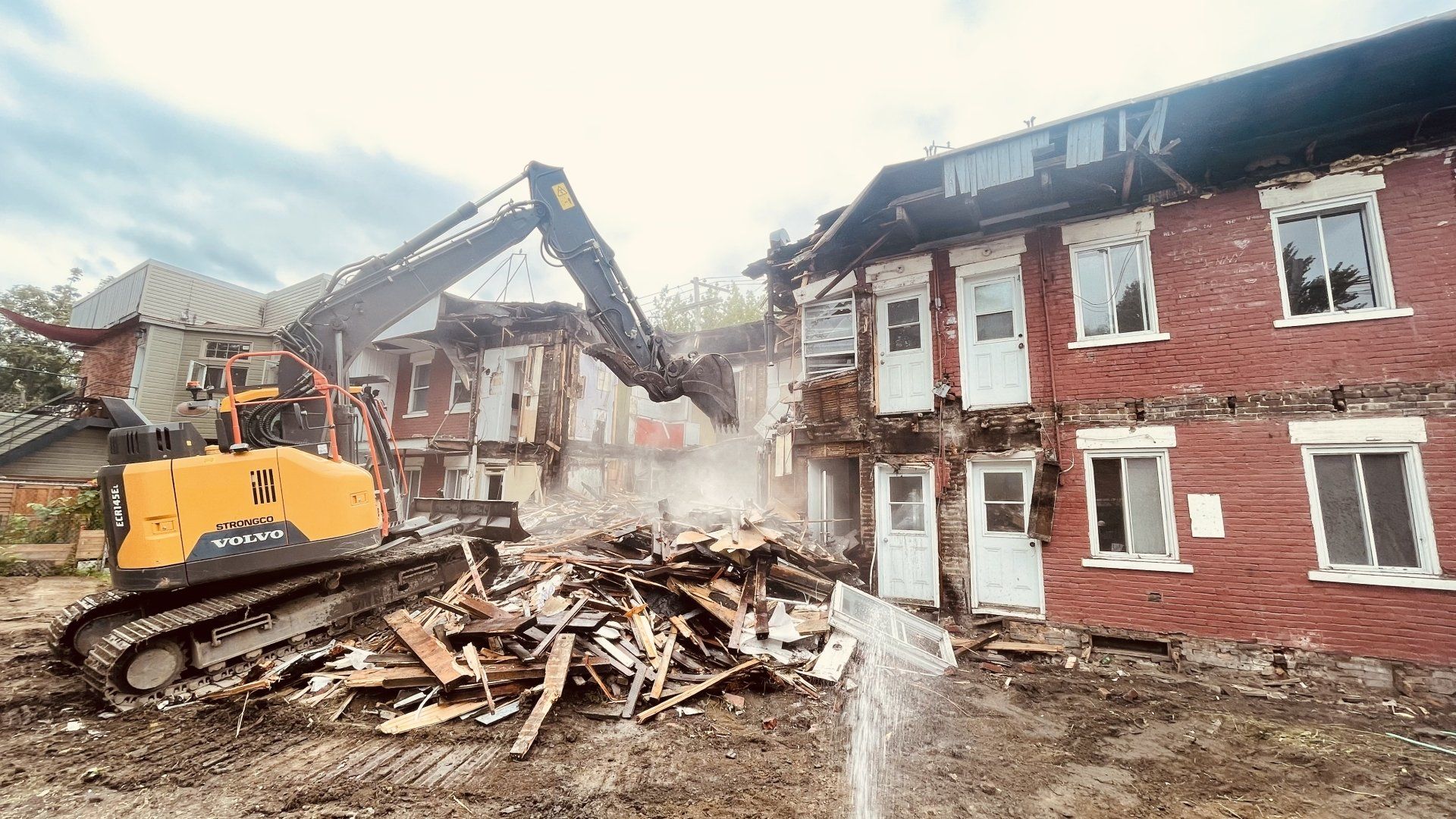 Une excavatrice démolit un bâtiment en briques, créant des débris.