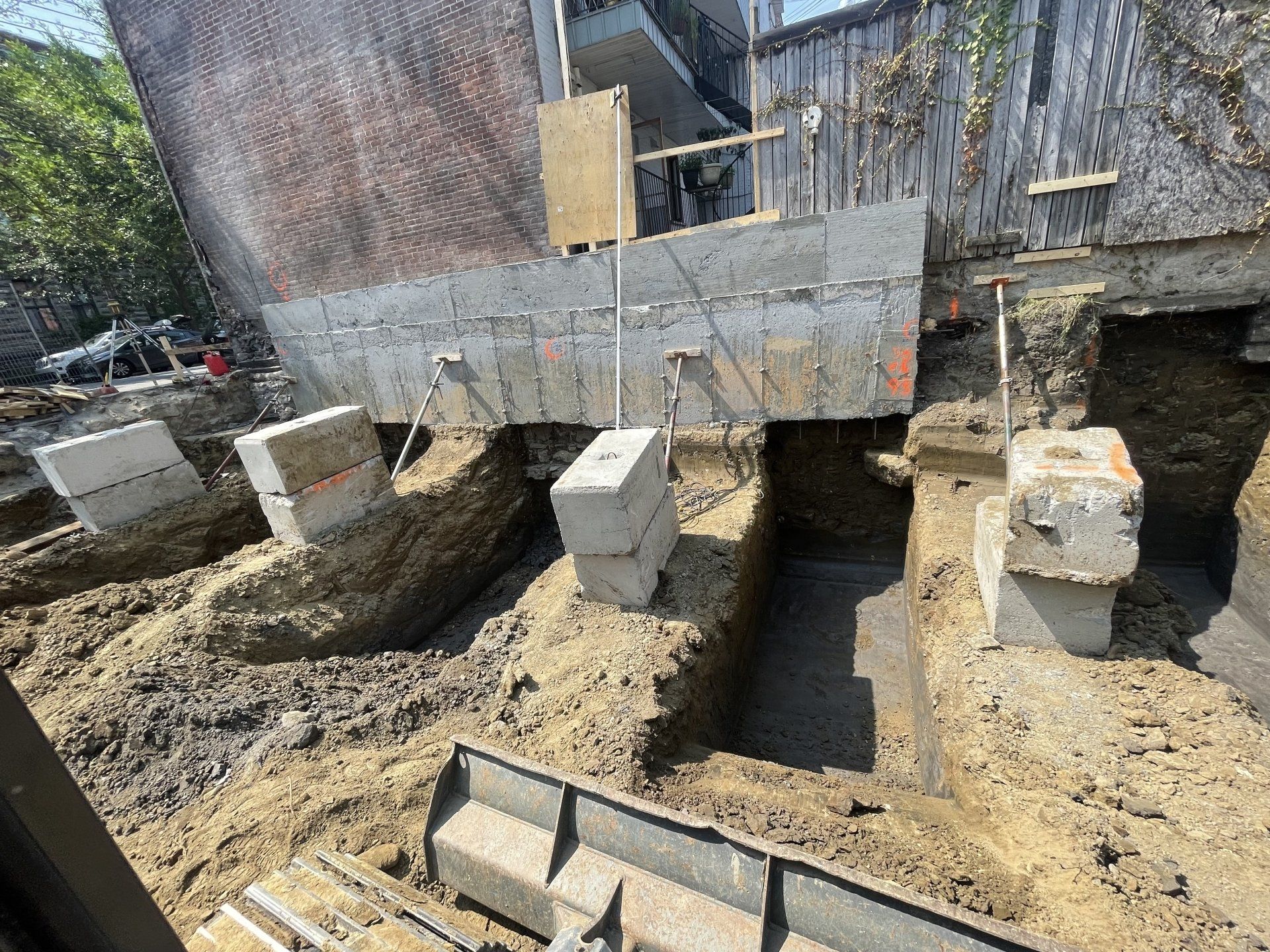 Des blocs de béton soutiennent les fondations d'un bâtiment en construction, dans un environnement extérieur avec de la terre excavée.