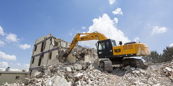 Une pelleteuse jaune démolit un bâtiment par une belle journée ensoleillée.