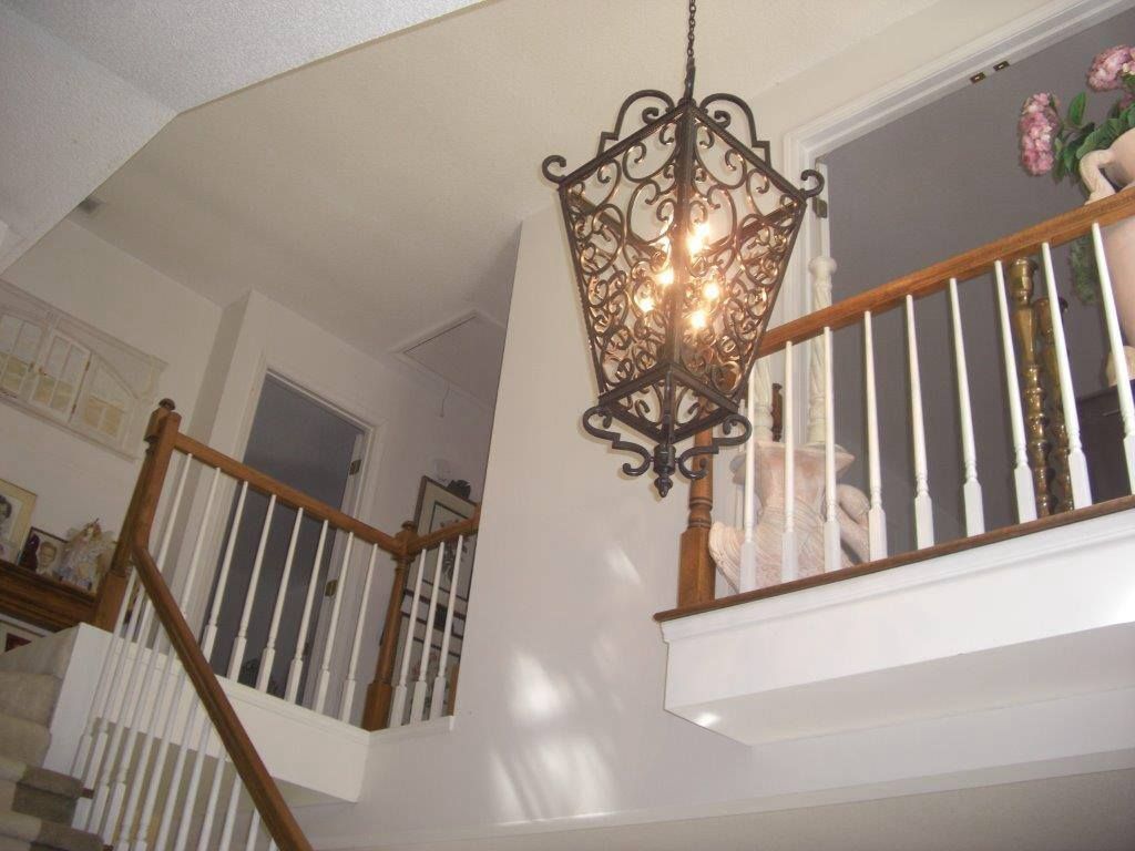 Staircase with white walls, wooden banister, and ornate black chandelier.