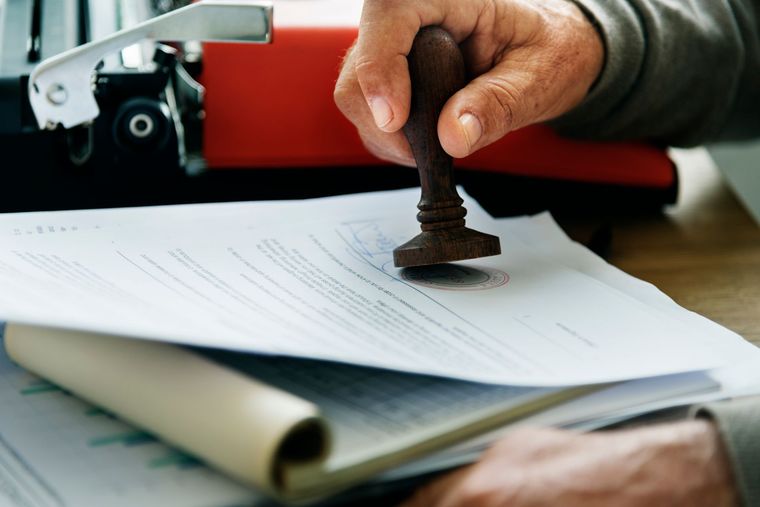Hand stamping a document beside a red typewriter on a desk