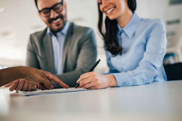 Two people in business attire signing a document at a table in a bright office