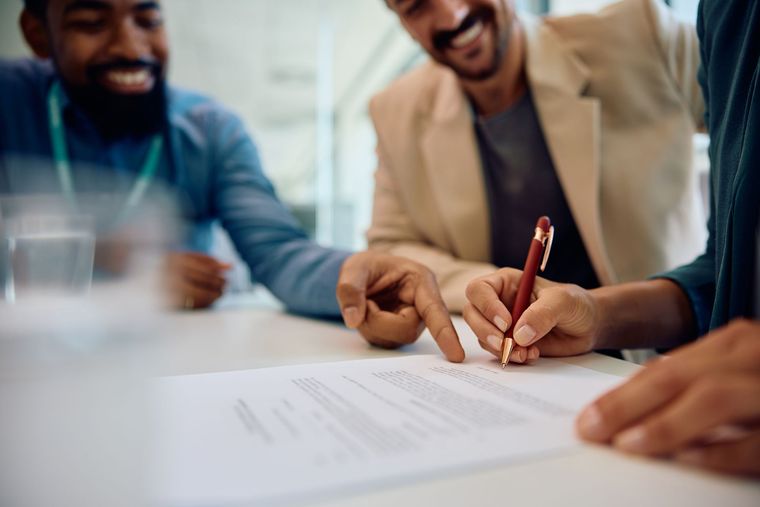 People reviewing and signing a document at a table in a bright office