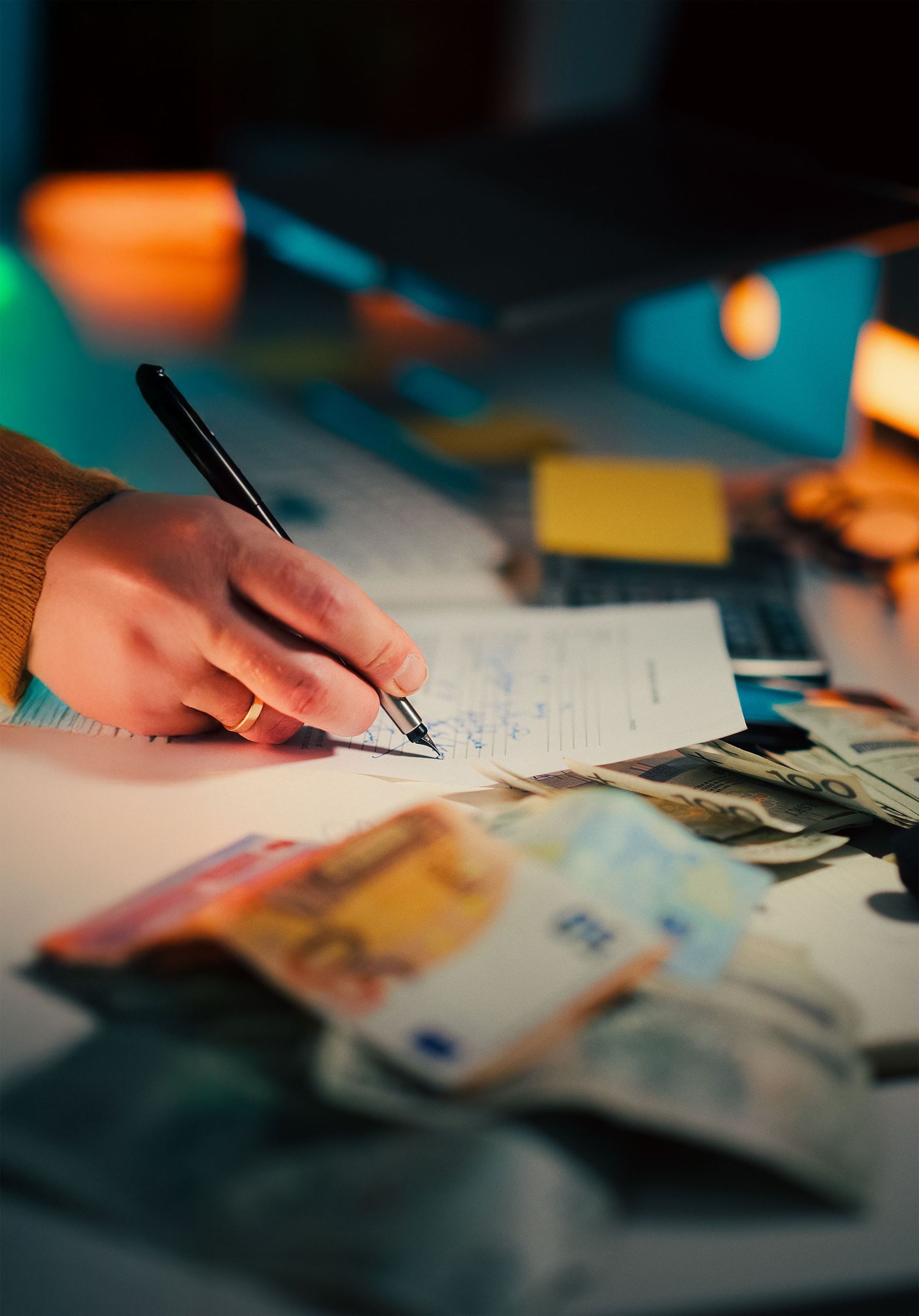 Hand writing on a notebook beside scattered currency and a blurred desk background