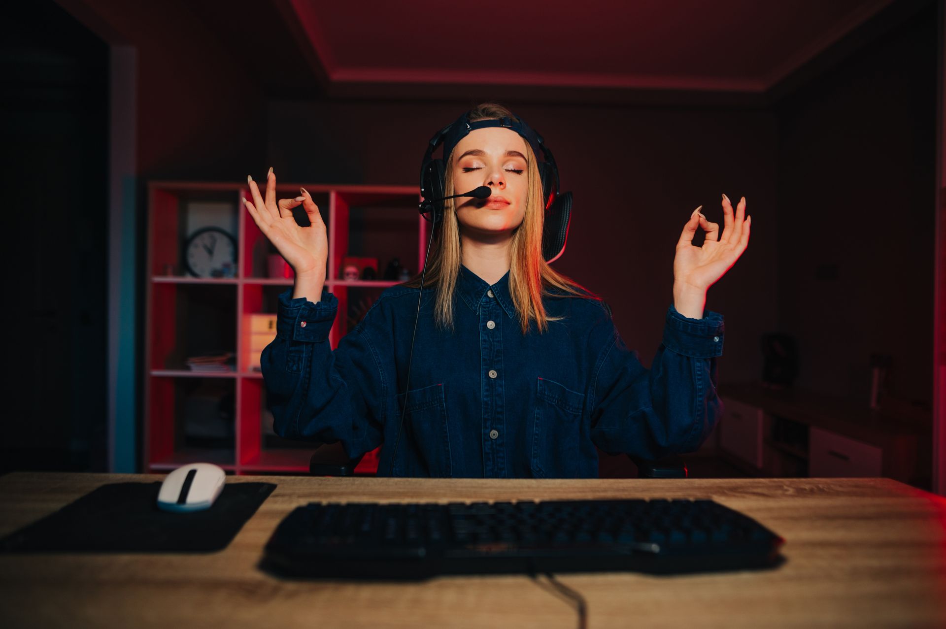 A woman with blonde hair wearing a backwards cap is sitting in an ergonomic gaming chair with her eyes closed and fingers touching, as she meditates between games.