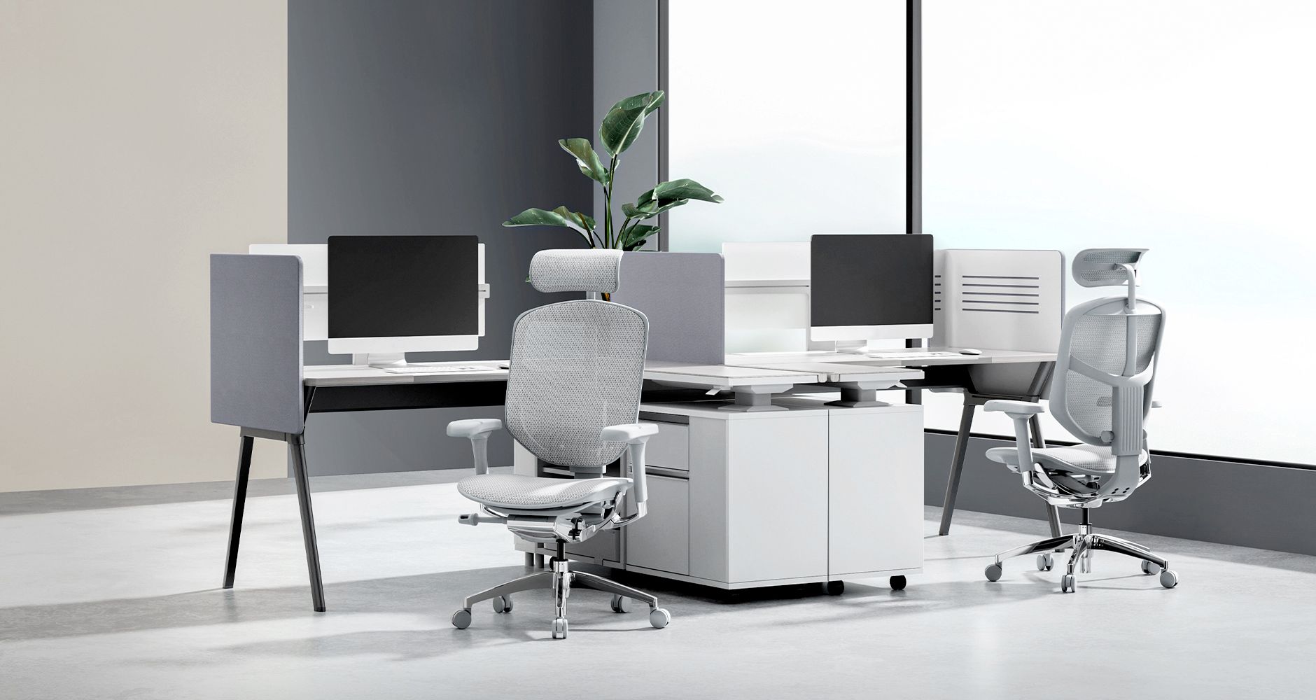 Two grey Enjoy Elite chairs are at two individual desks and booths. On the desks are monitors and keyboards. Between the desks is a storage unit. In the background is a large window to let in natural light.