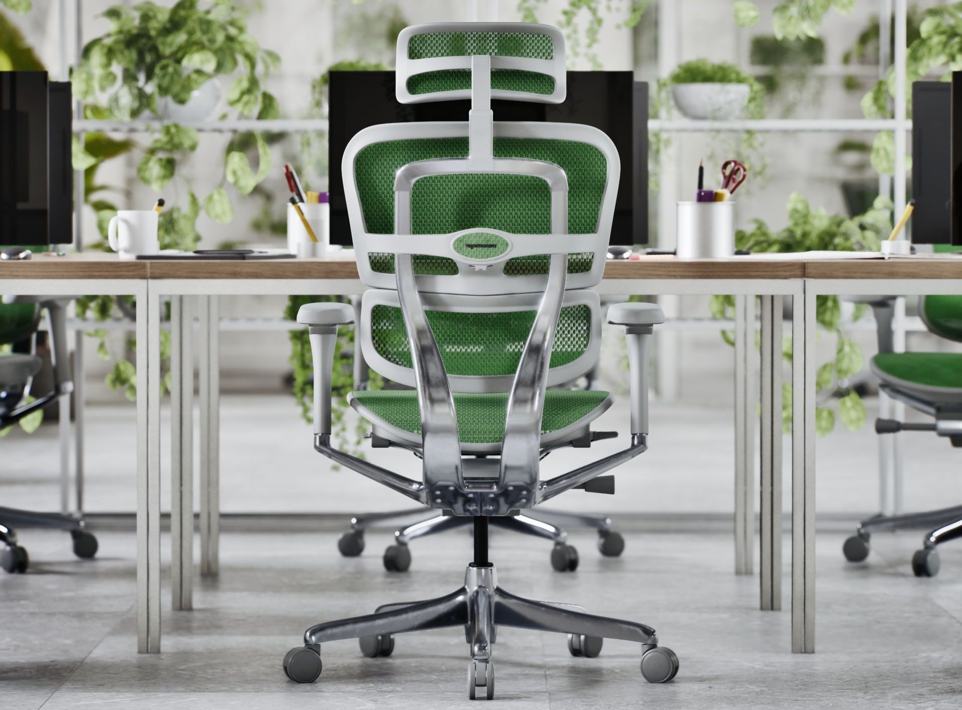 Ergihuman Elite G2 mesh office chair with green mesh and grey frame facing a bench desk with monitors, pens, mugs and books. The office is light and airy, full of vibrant greenery.