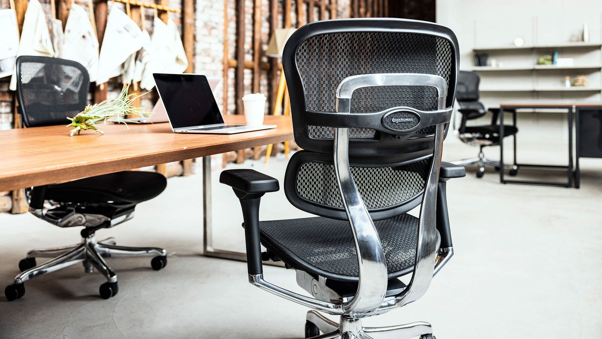 Close up of the back of an ergonomic black mesh chair at a table in a relaxed office space.