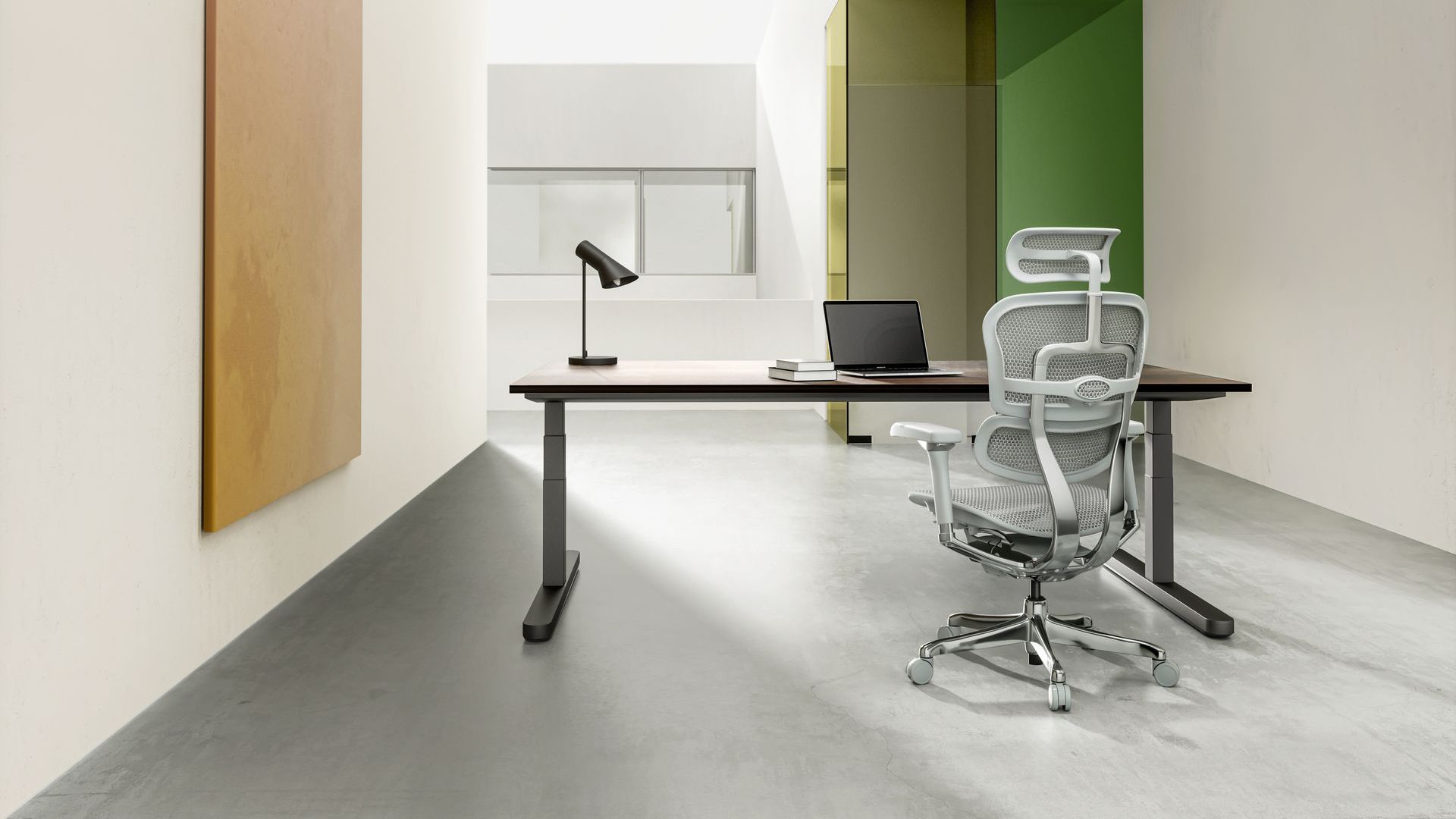 Grey on grey Ergohuman Elite chair in an open office space, situated at a desk. On the desk is a laptop, two books and a black lamp.