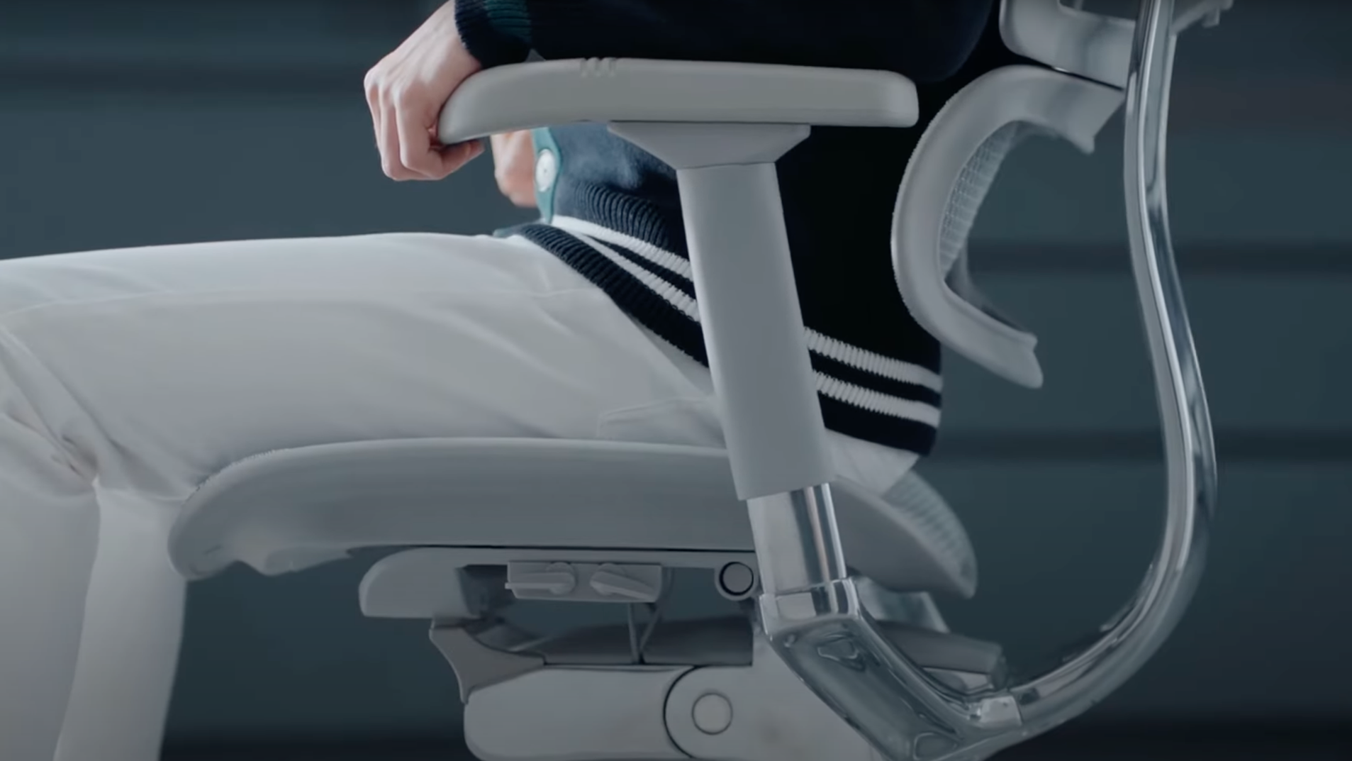 Close up of a man sitting in a light grey mesh office chair's. Focus on the chair's lever to adjust seat tilt. Chair for creative work.