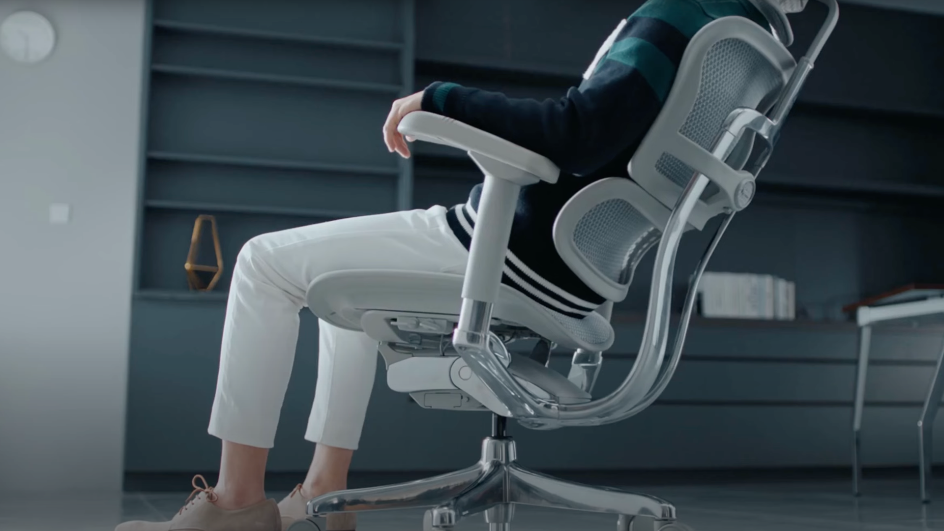 Close up of a man reclining in a light grey mesh office chair.