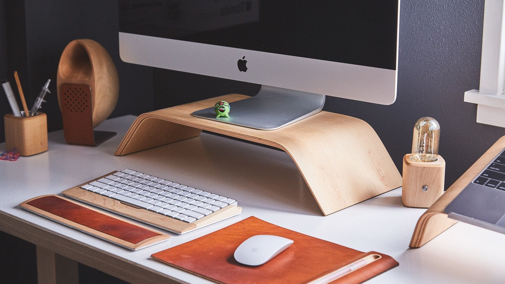 Close up of a desk with a monitor stand, iMac, keyboard, magic mouse, mousepad and a wrist pad.
