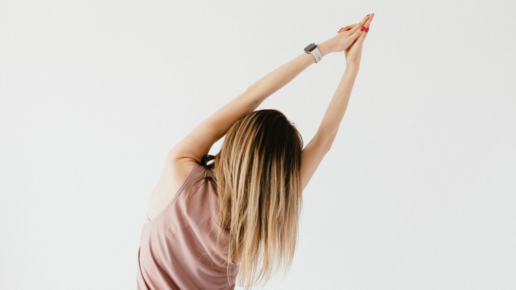 A woman standing stretching to the side in front of a white wall. She has long blonde hair.