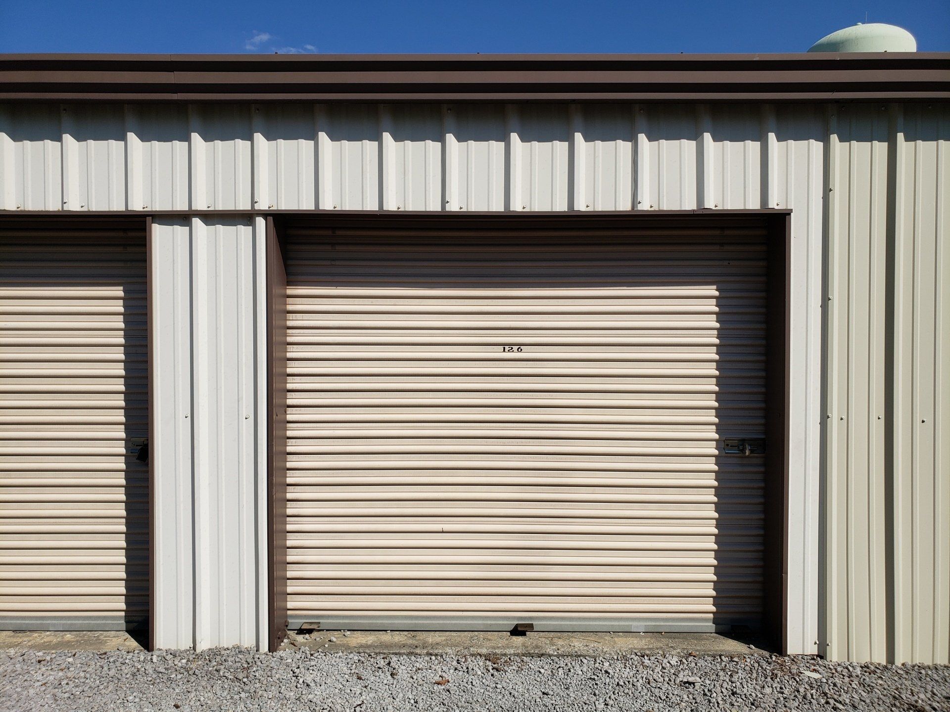 Metal storage units with closed beige roll-up doors beneath a blue sky