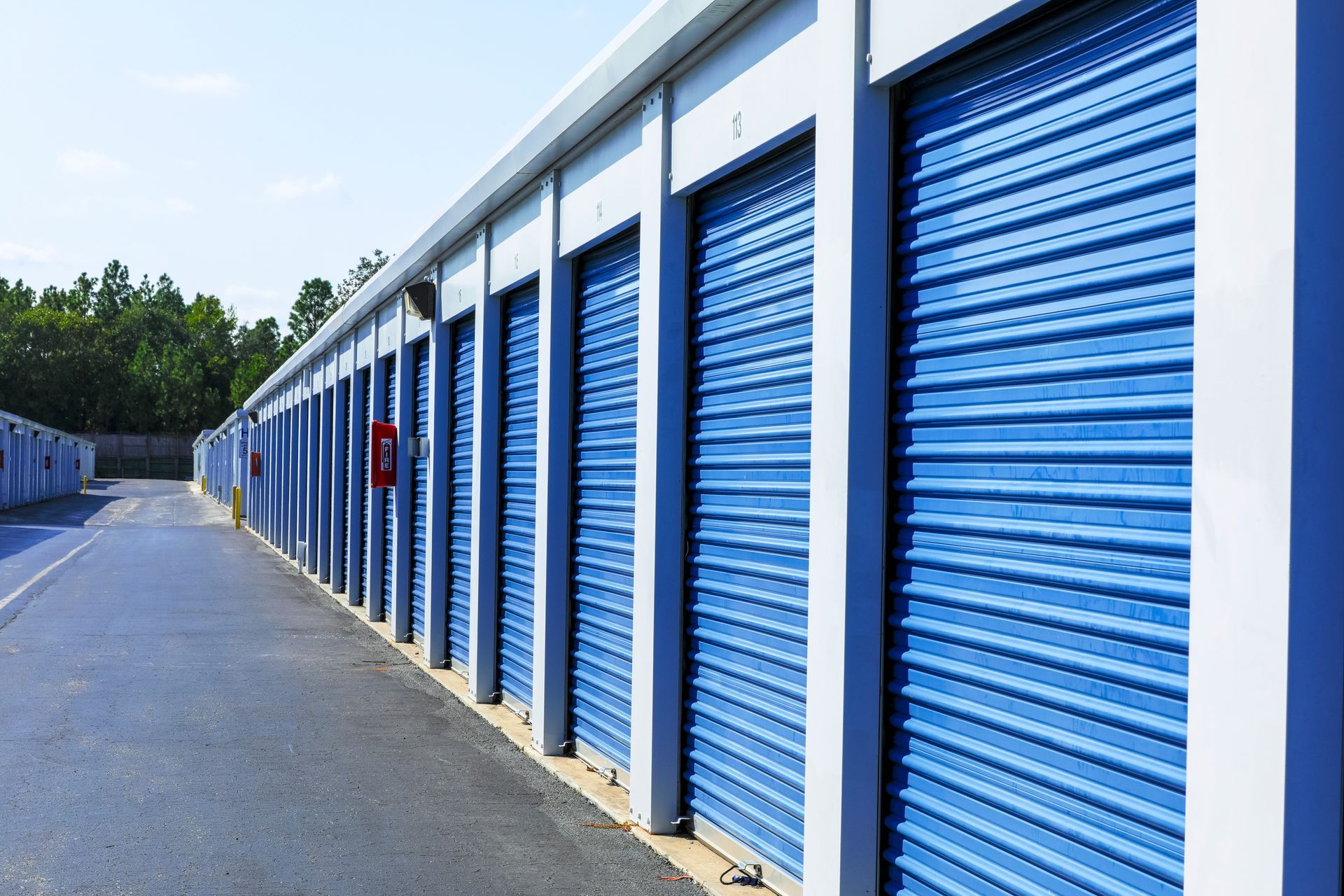 Row of blue roll-up doors at an outdoor self-storage facility.
