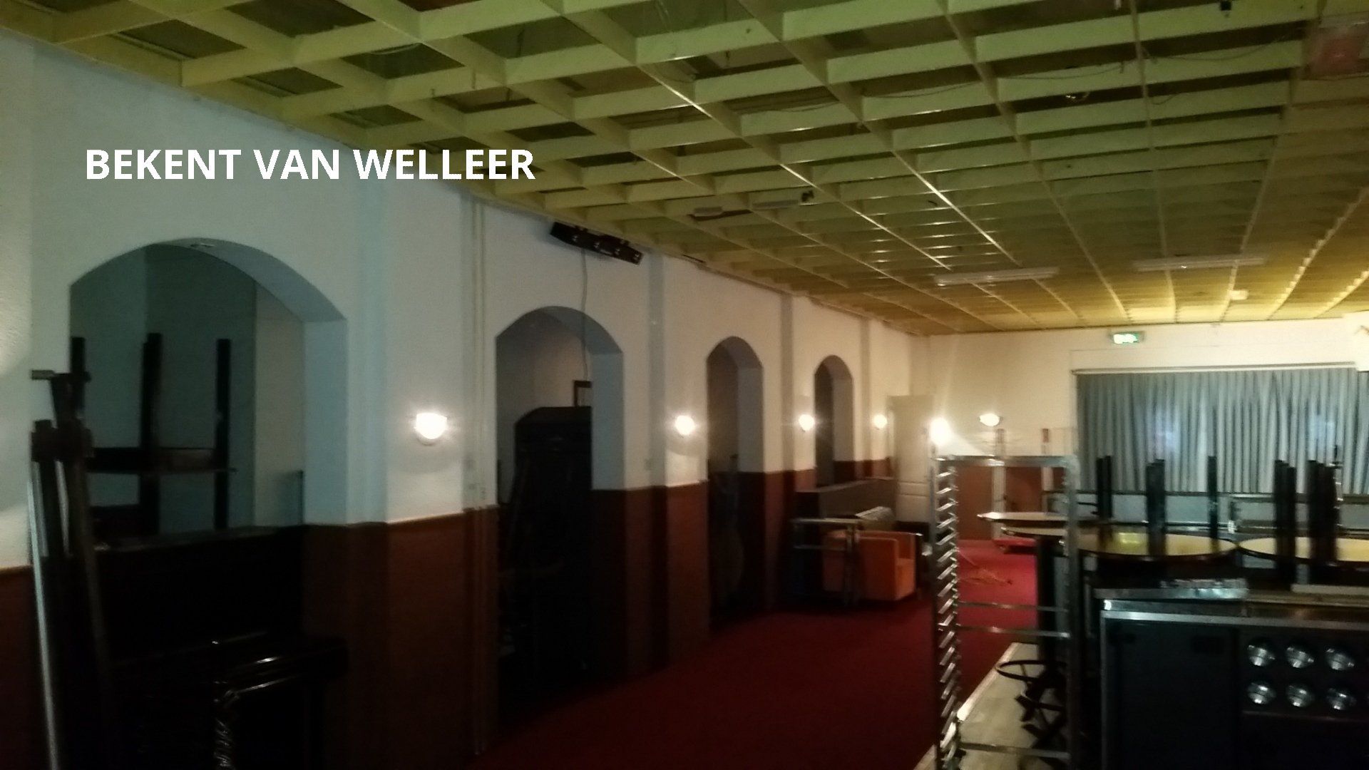 Interieurfoto van een schemerig verlichte hal met gewelfde deuropeningen, een rode loper en een decoratief rasterplafond.