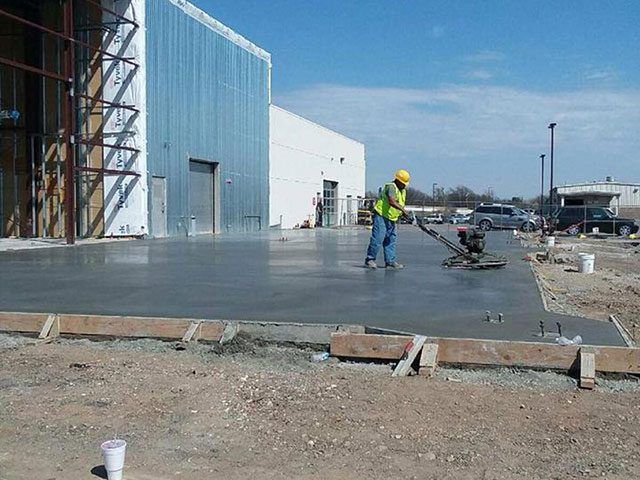 A man is working on a concrete floor in front of a building A man is working on a concrete floor in front of a building