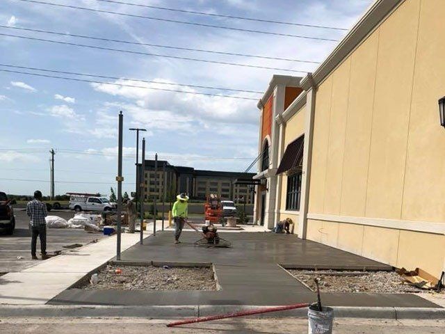 A group of people are working on a sidewalk in front of a building. A group of people are working on a sidewalk in front of a building.
