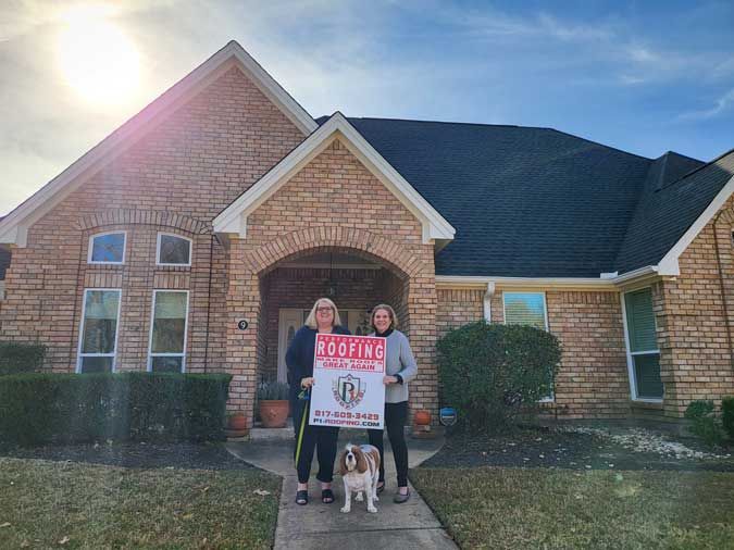 Two women and a dog are standing in front of a brick house holding a sign.