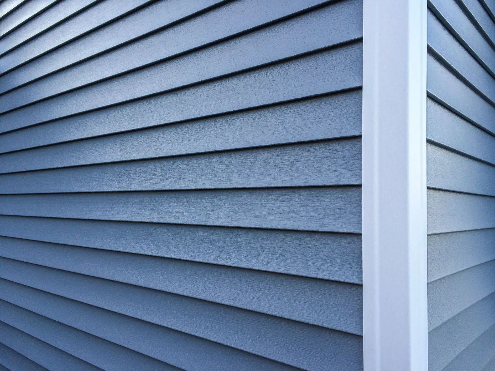Blue horizontal vinyl siding on a house exterior meeting at a white corner post.