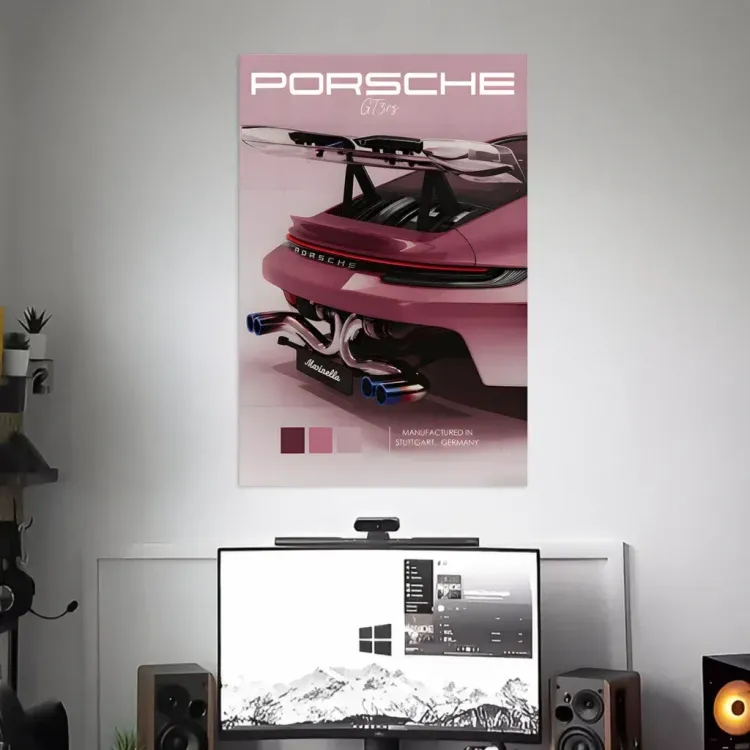 Porsche poster above a desk with a monitor, speakers, and a small plant in a minimalist room