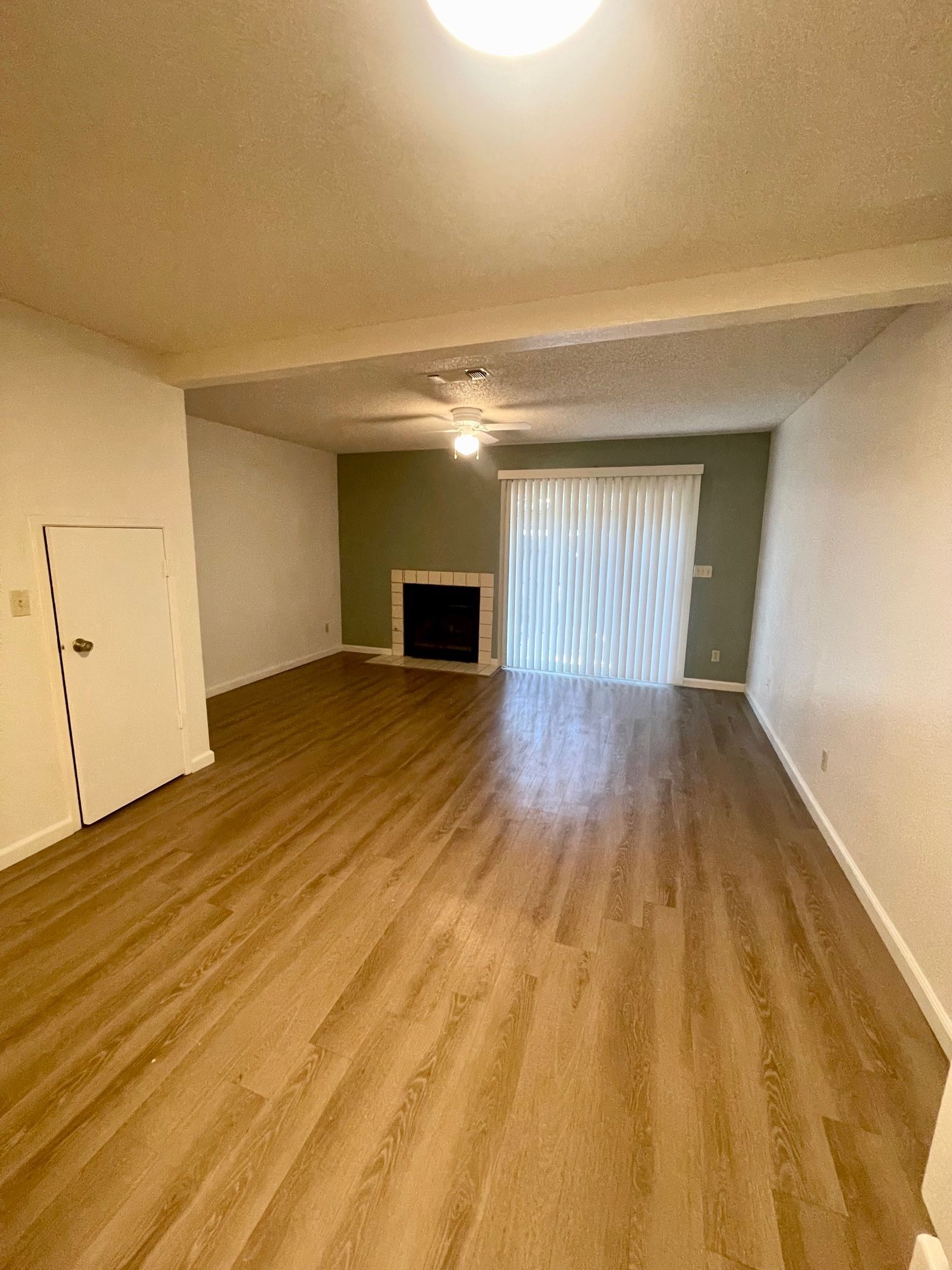 Empty living room with hardwood floors, fireplace, and sliding glass door.