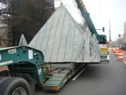 A large pyramid is being moved down a street by a crane
