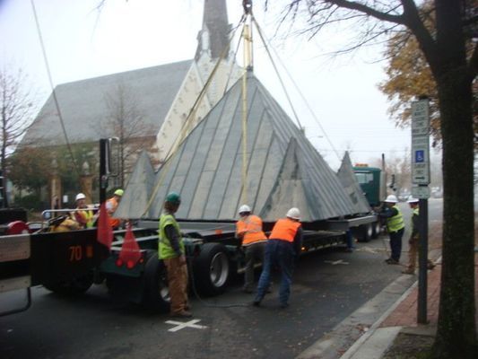 A large pyramid is being lifted by a crane in front of a church