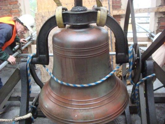 A man in a hard hat stands next to a large bell