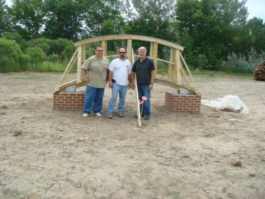 Three men are standing in front of a wooden bridge