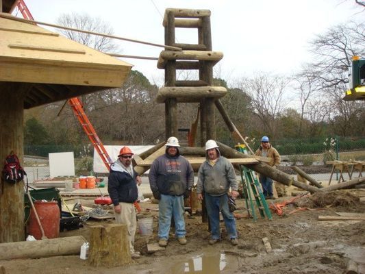 Three men wearing hard hats are standing in a muddy area
