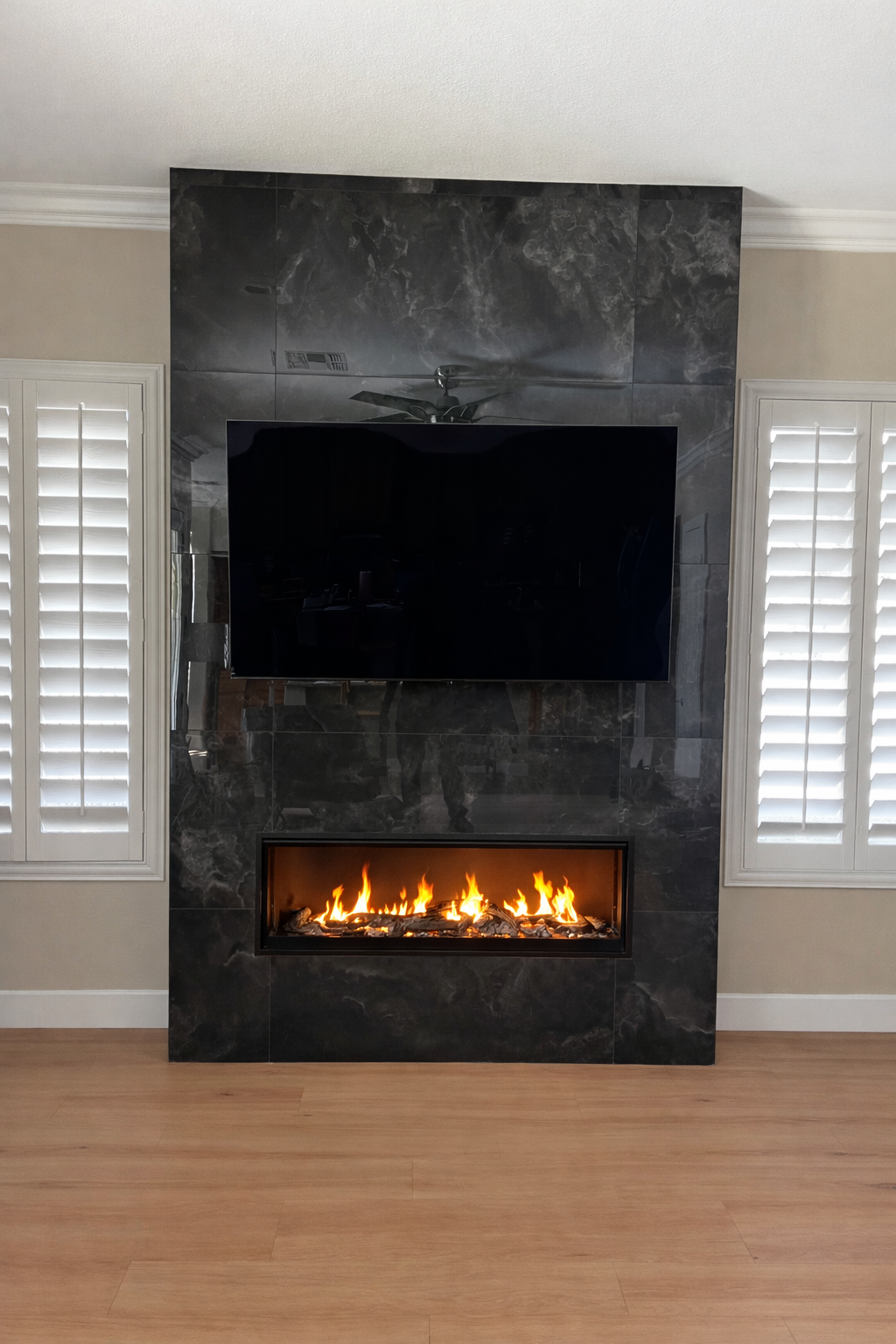 Modern living room with black marble fireplace, wall-mounted TV, and lit electric fire below